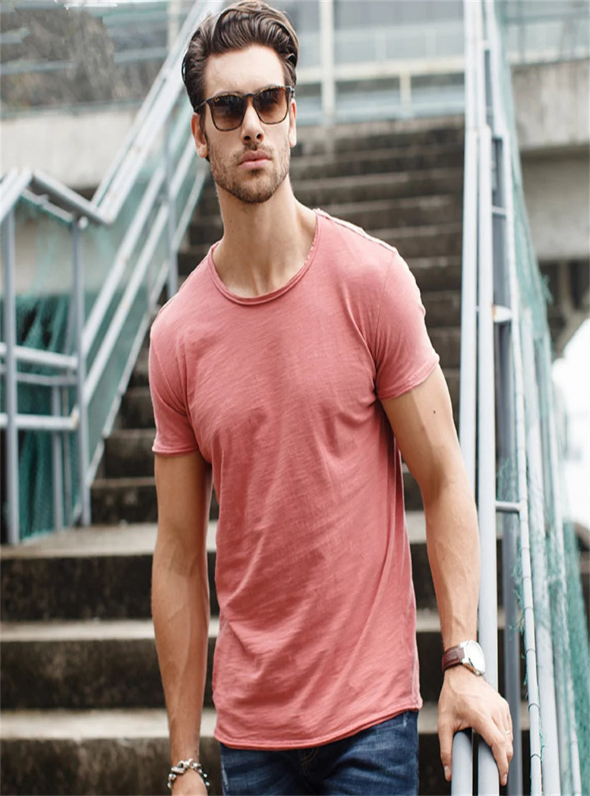 Man wearing a pink t-shirt and sunglasses standing on outdoor steps.