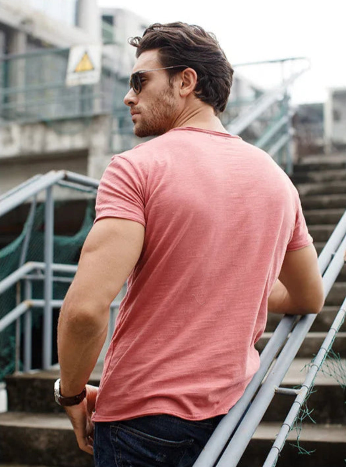 Man wearing a pink t-shirt standing outdoors near stairs