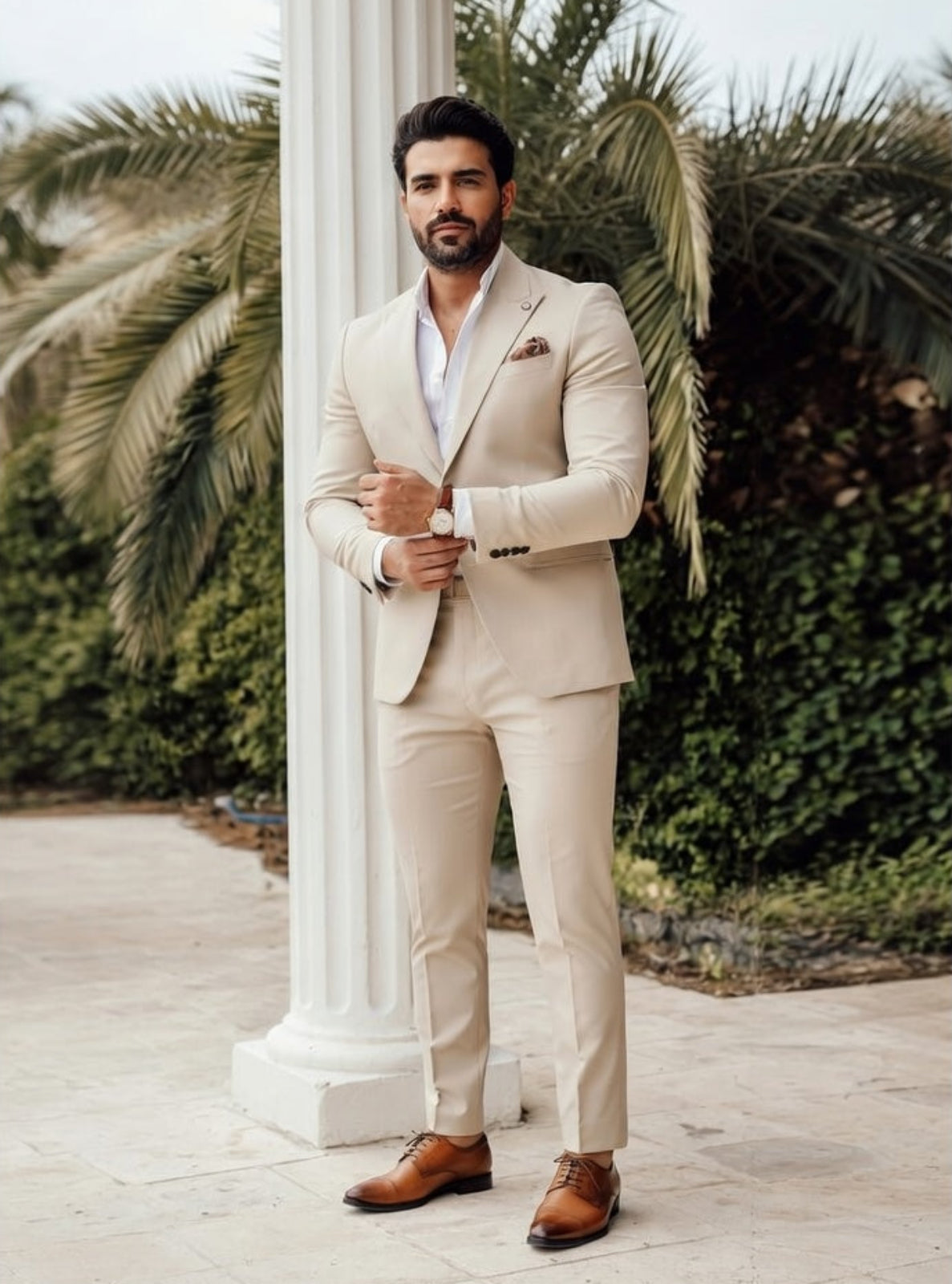 Man in a beige suit standing outdoors with palm trees in the background