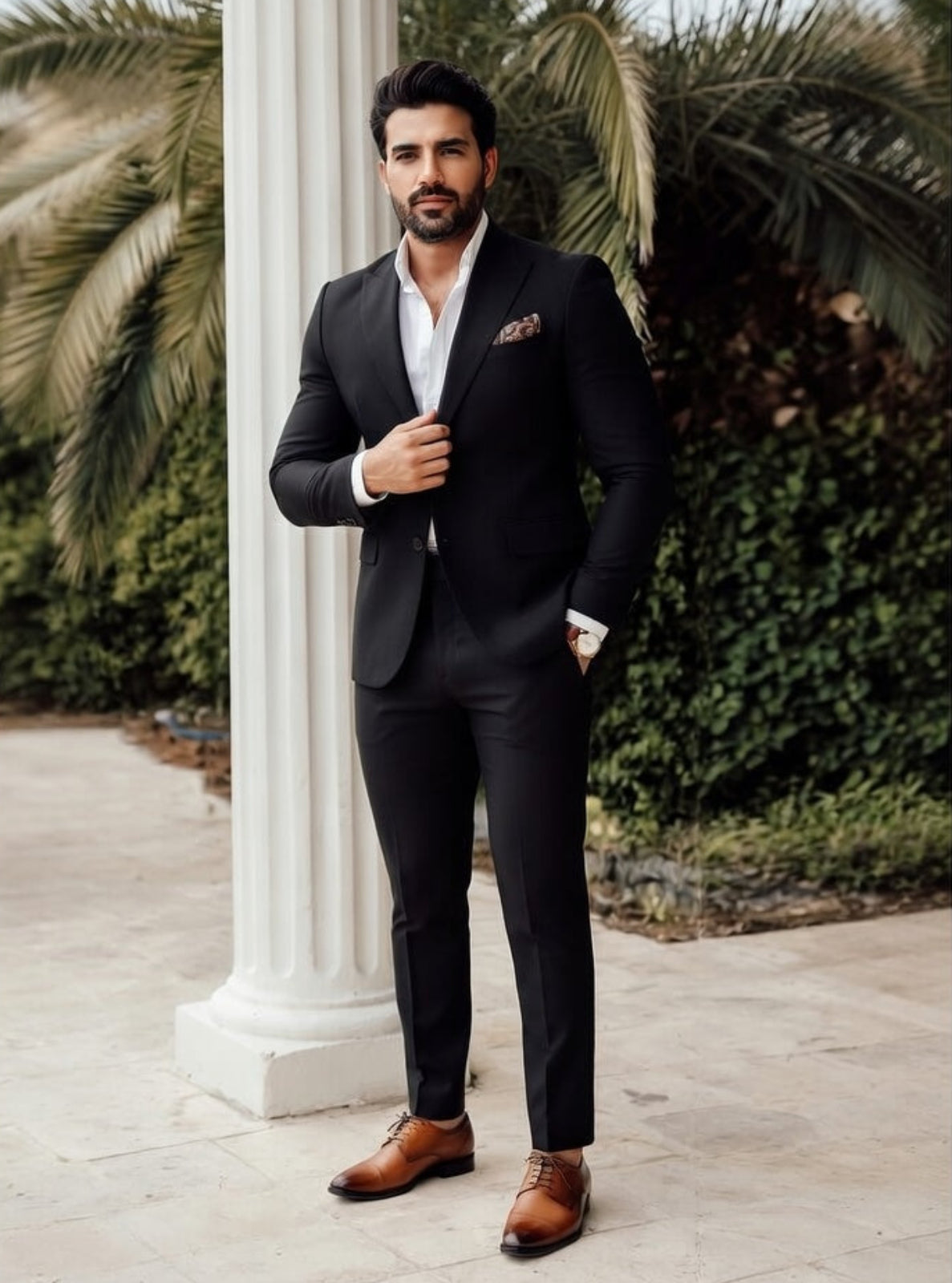Man in a black suit standing outdoors with palm trees in the background