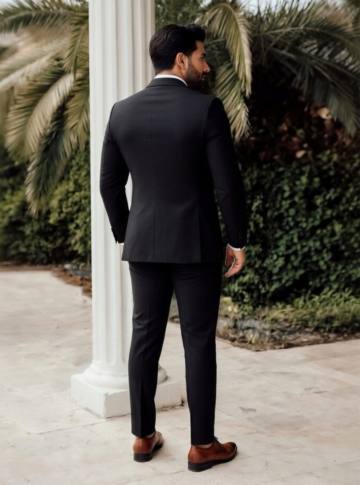 Man in a black suit standing outdoors with palm trees in the background