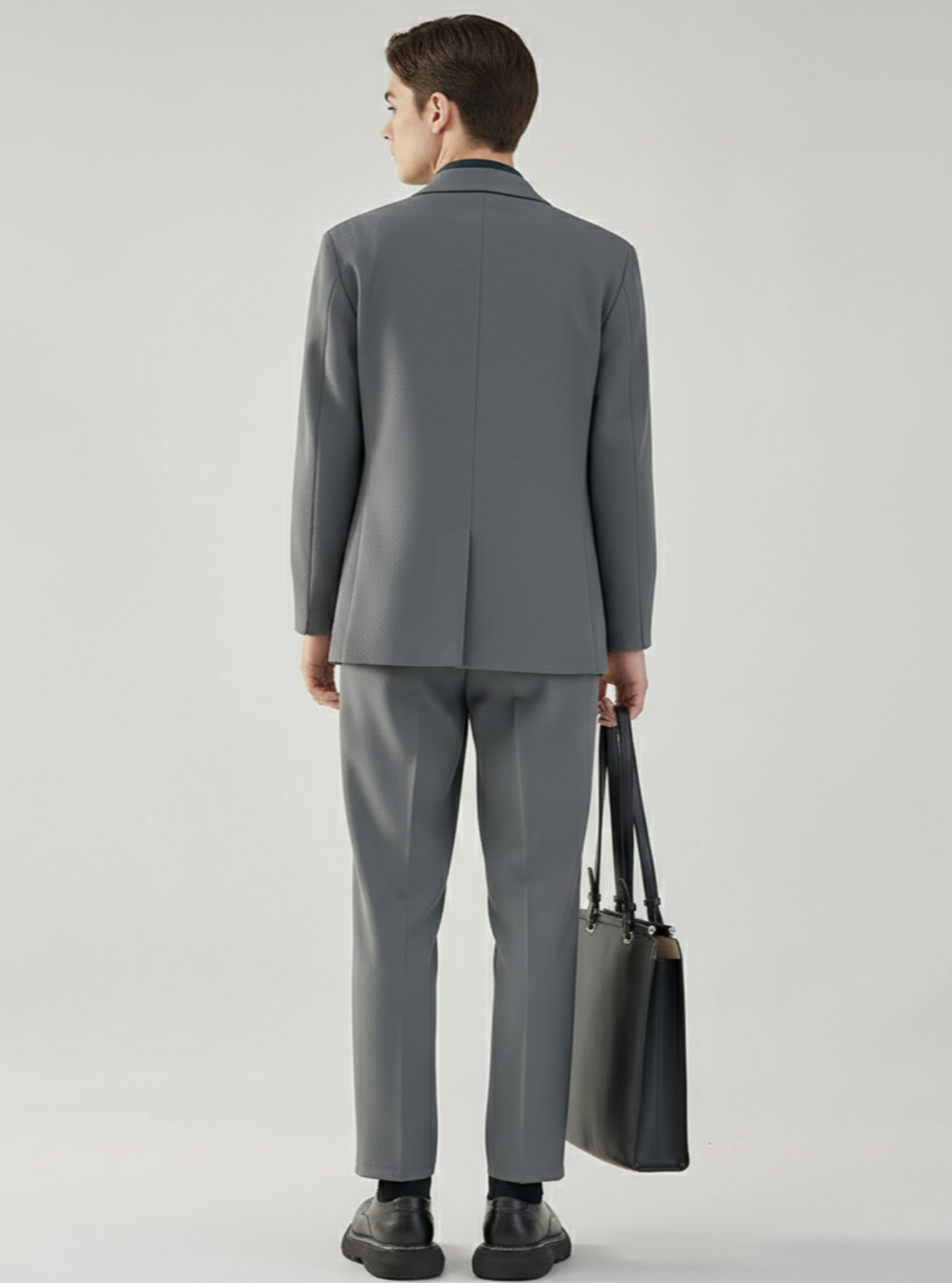 Man wearing a gray suit holding a black bag on a light gray background