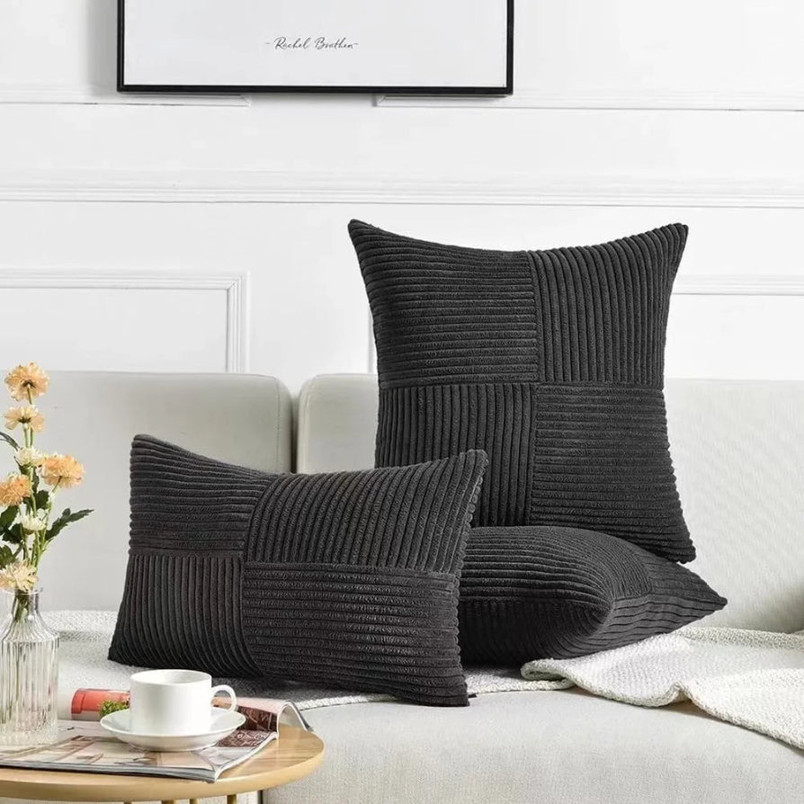 Dark gray textured pillows on a light-colored sofa with a small table and flowers in the foreground.