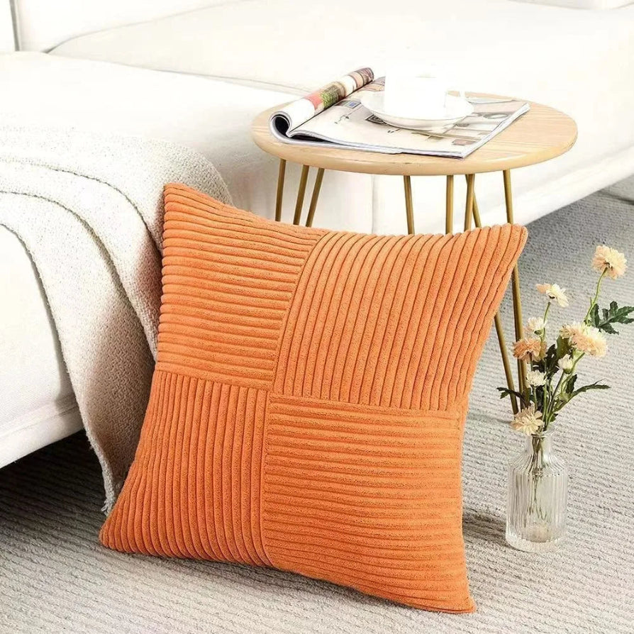 Orange textured pillow on a couch with a side table and flowers in the background