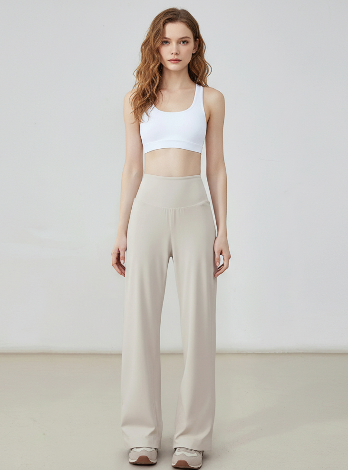 Woman wearing a white tank top and beige pants against a plain background