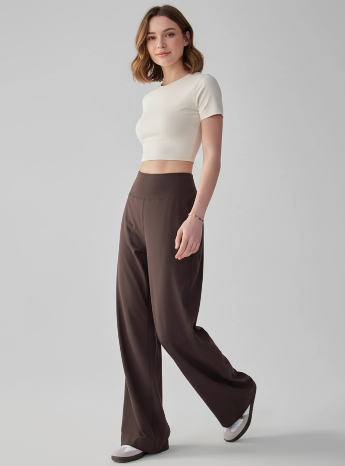 Woman wearing a white crop top and brown wide-leg pants on a gray background