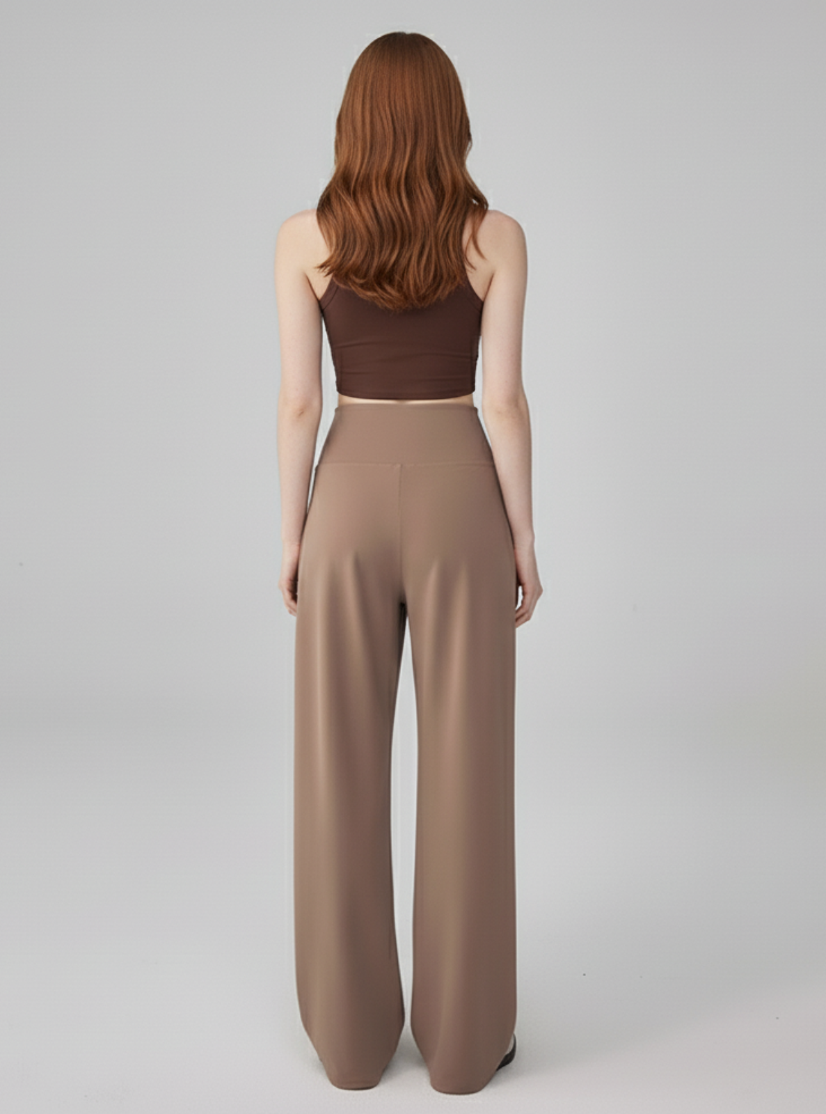 Woman wearing a brown top and beige pants on a gray background