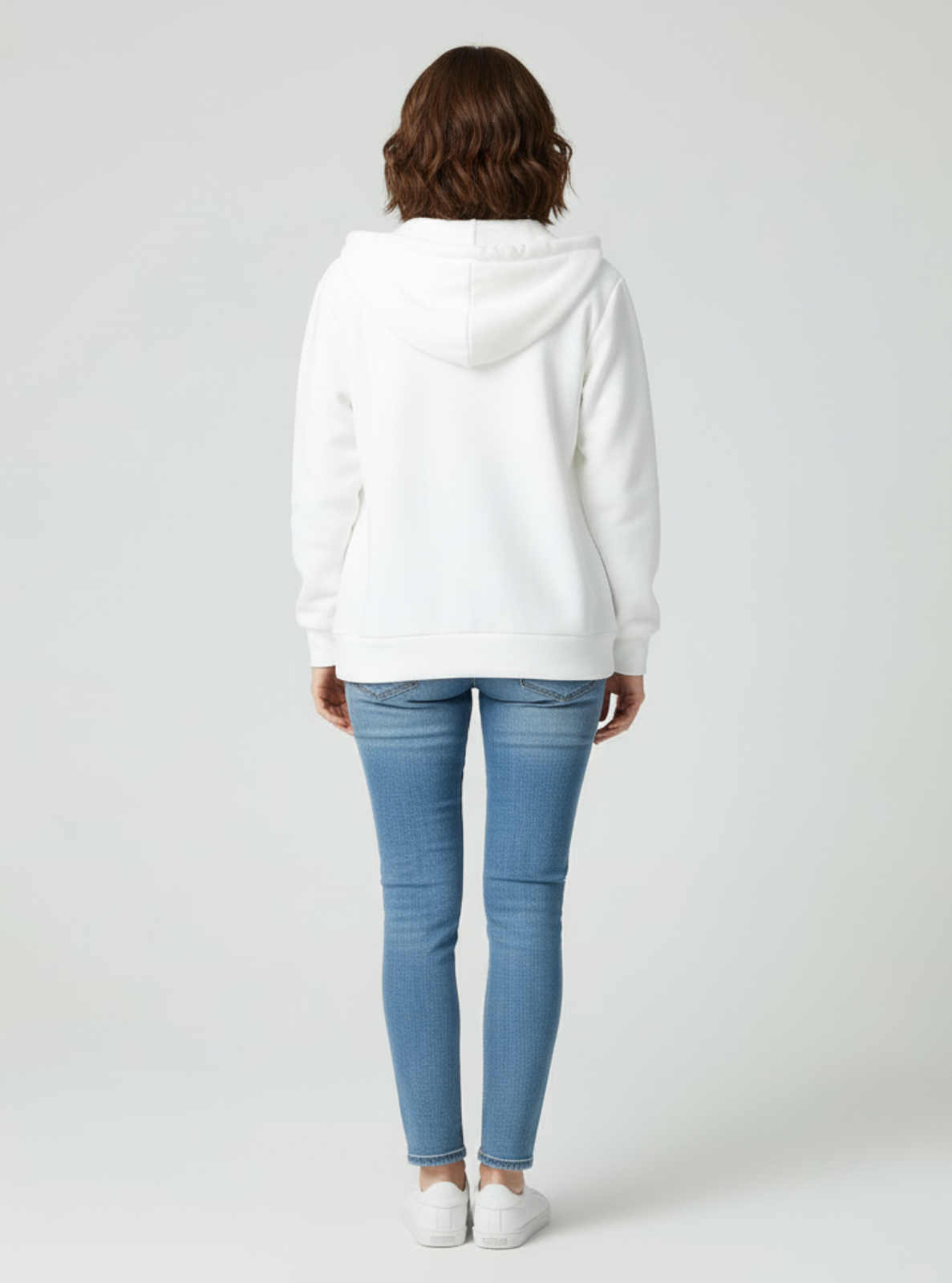 Person wearing a white hoodie and light blue jeans on a plain background
