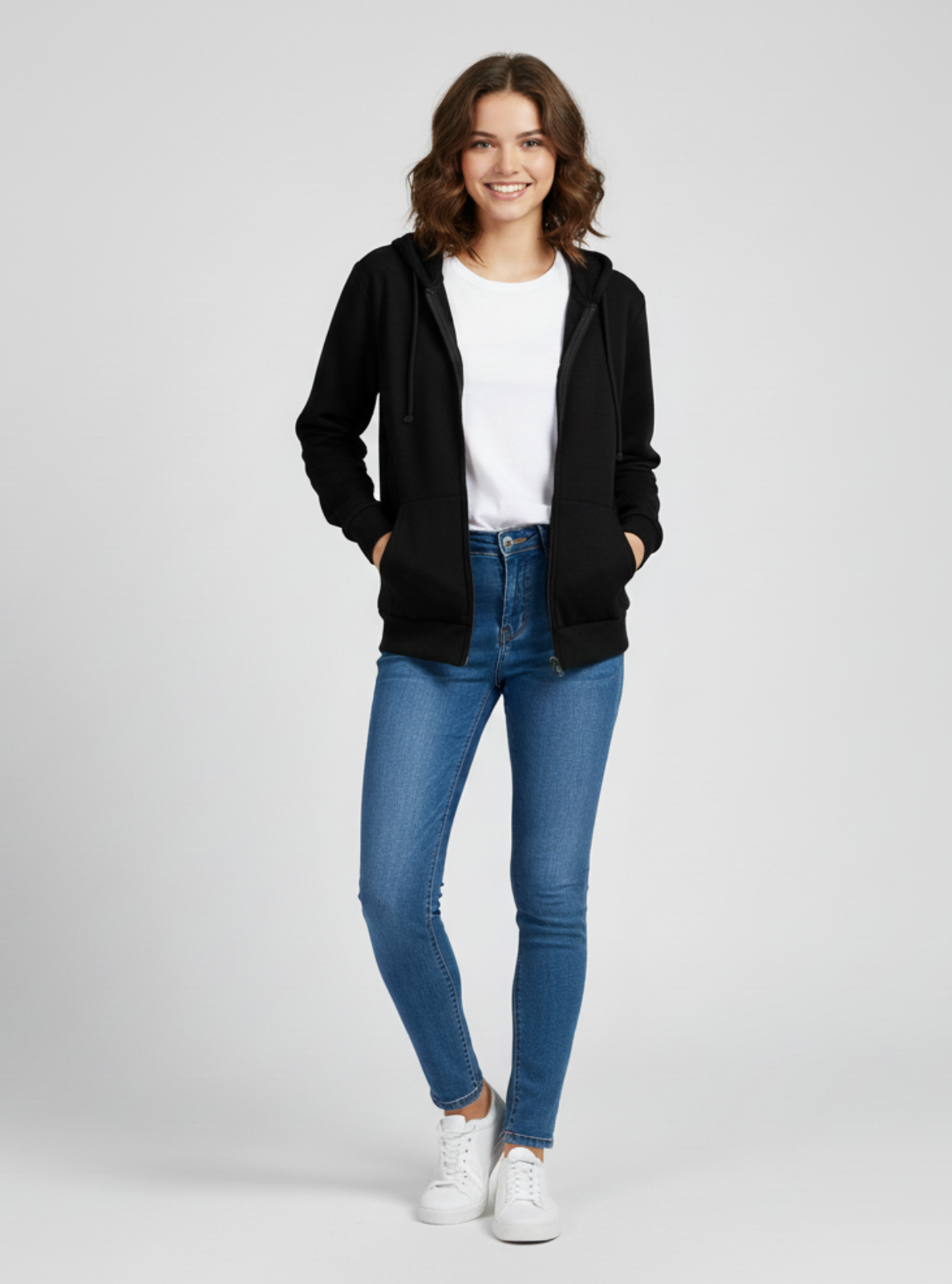 Woman wearing a black jacket, white shirt, blue jeans, and white sneakers on a light gray background