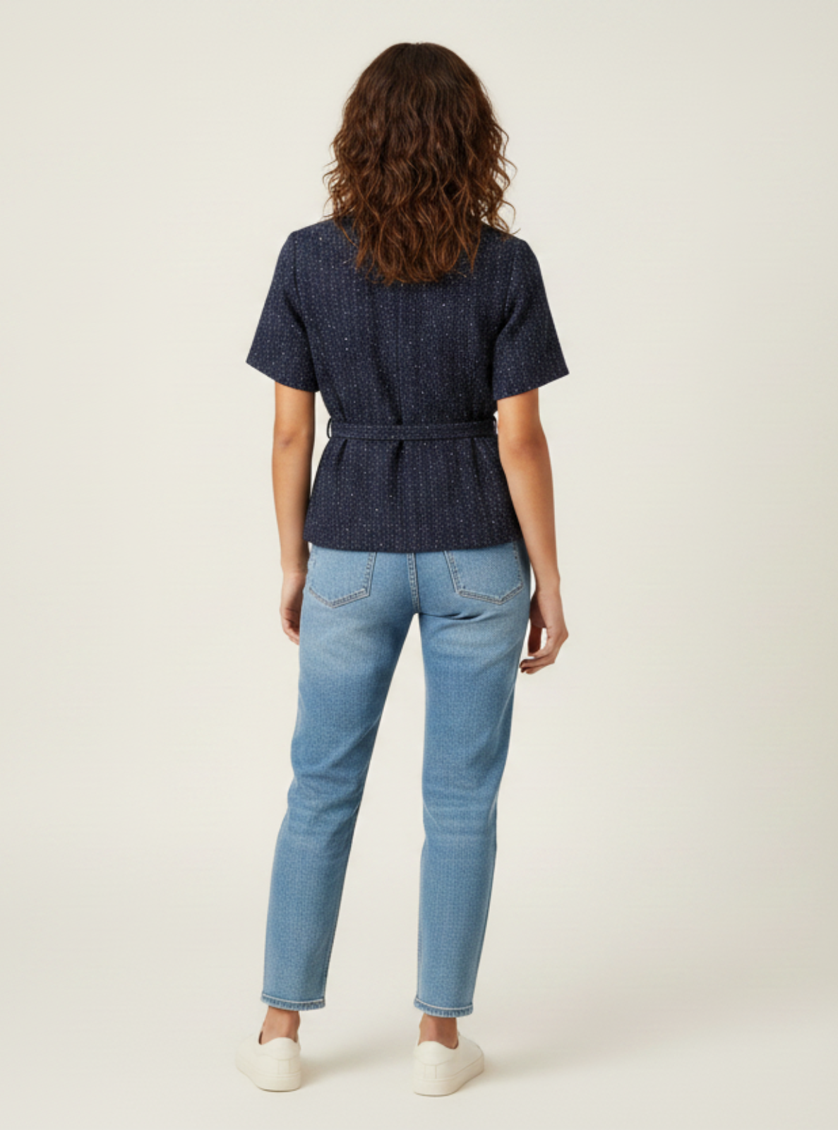 Woman wearing a dark blue top and light blue jeans on a white background