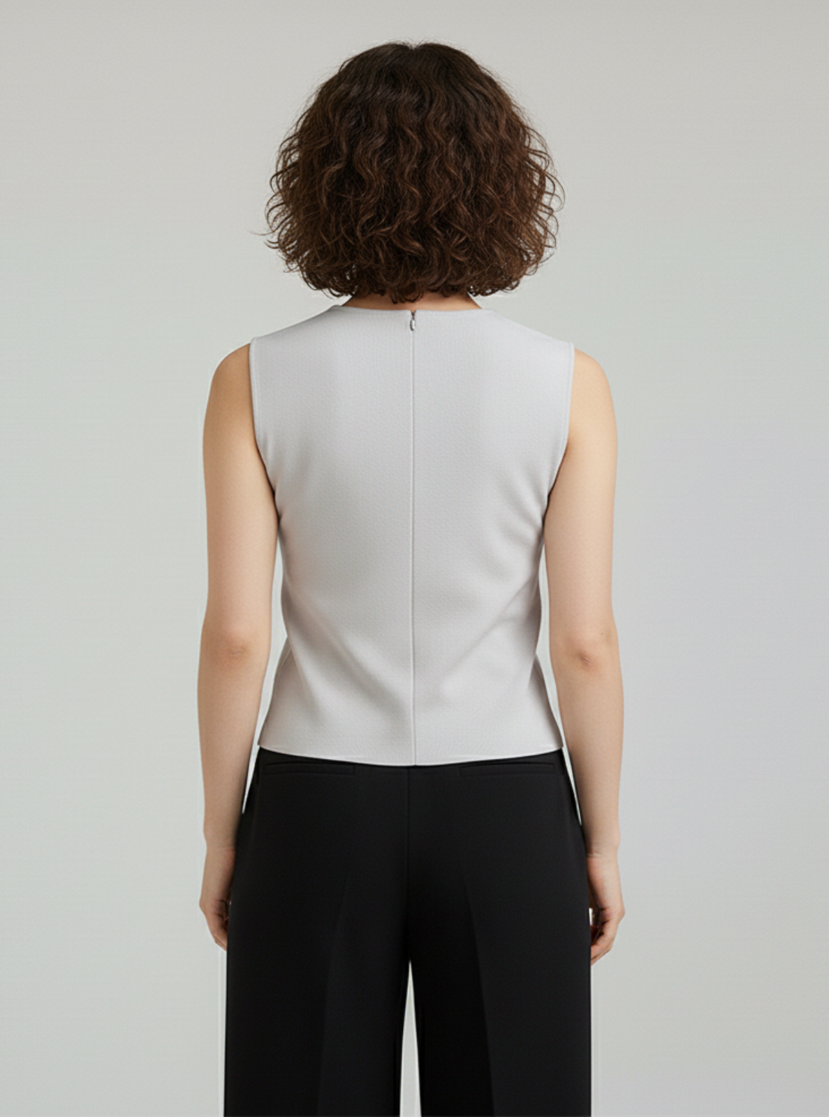 Person wearing a light gray sleeveless top and black pants on a plain background