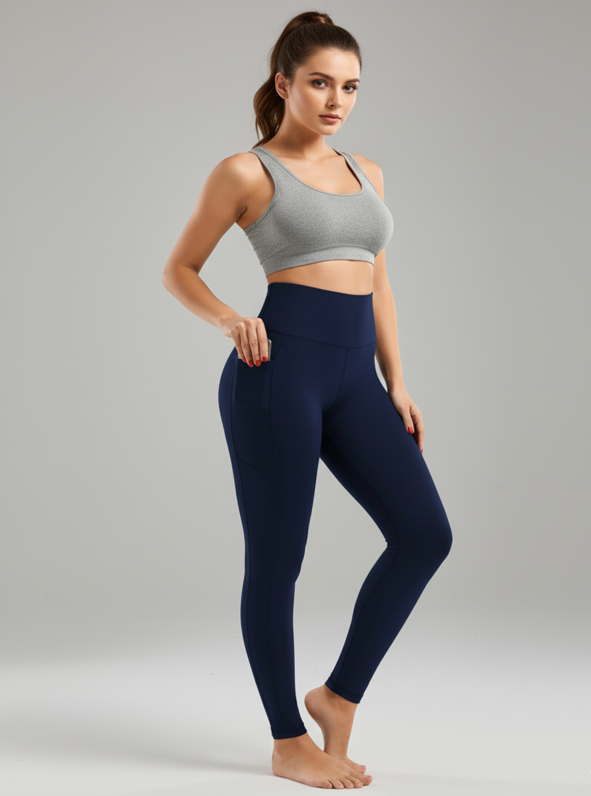 Woman wearing a gray sports bra and navy leggings on a gray background
