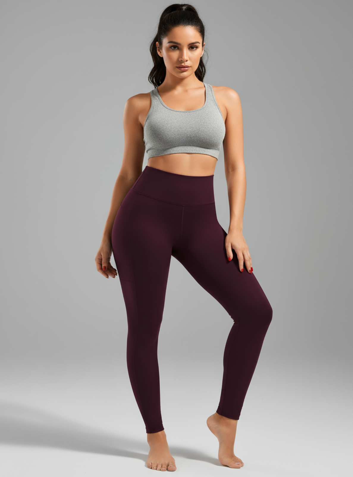 Woman wearing a gray sports bra and maroon leggings on a gray background