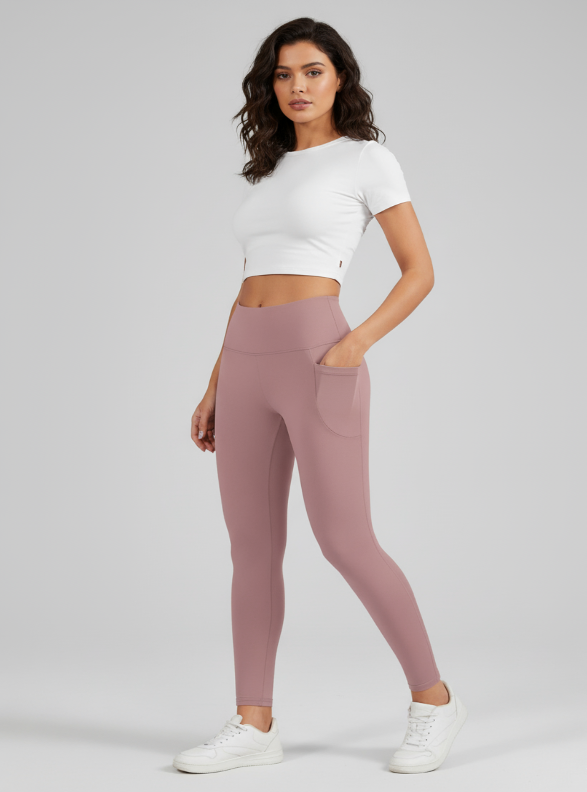Woman wearing a white crop top and pink leggings on a gray background