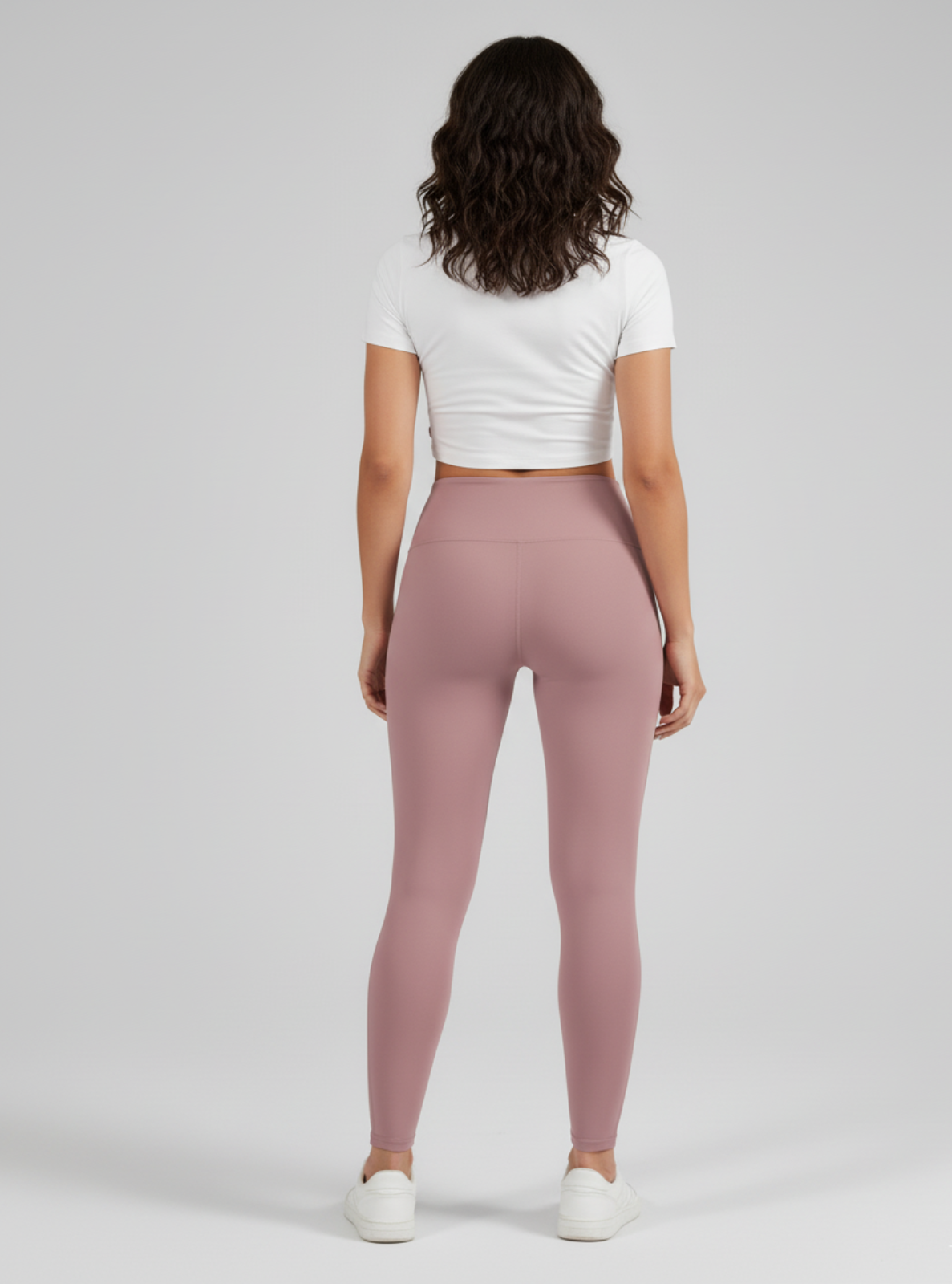 Person wearing pink leggings and a white crop top on a gray background