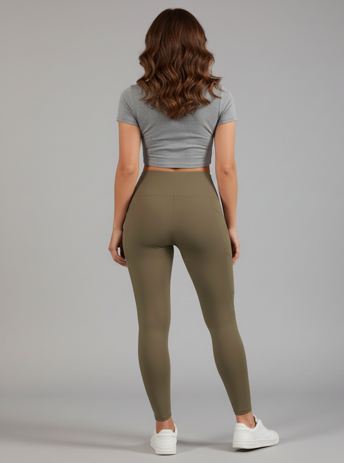Woman wearing a gray crop top and olive green leggings on a plain background