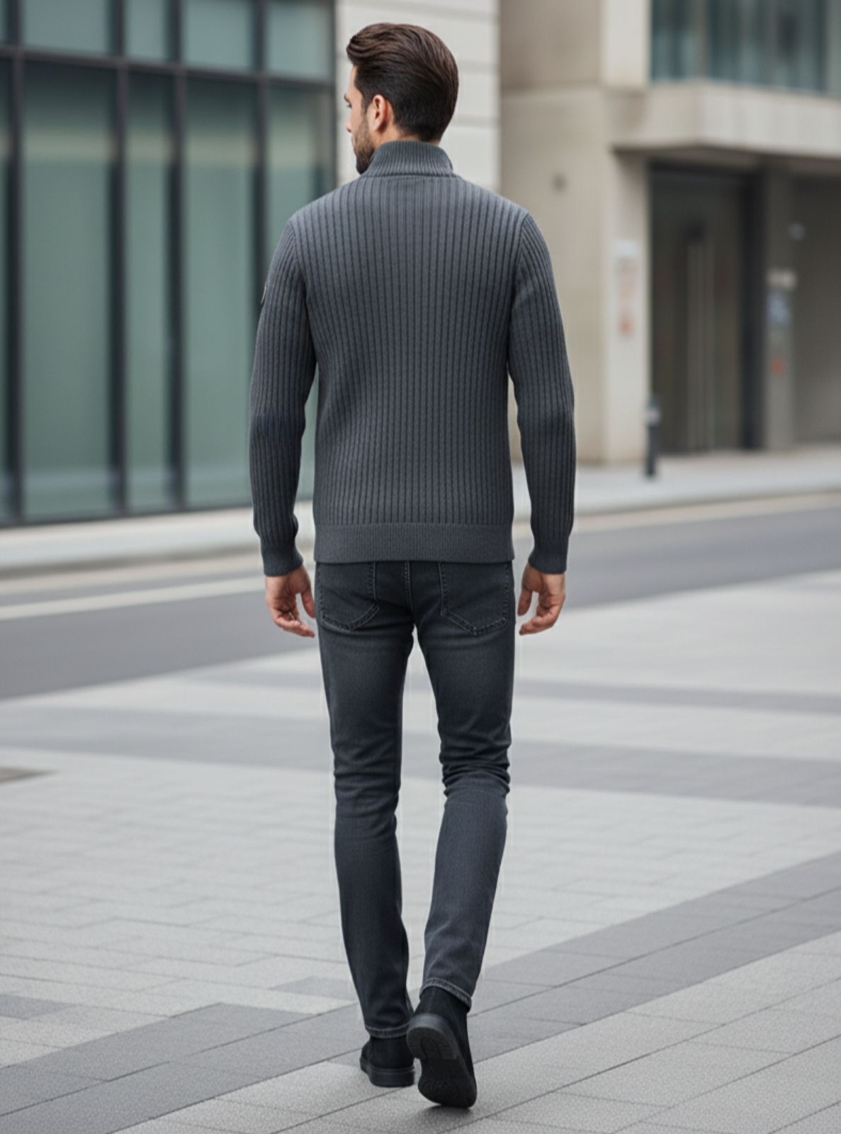 Man wearing a gray sweater and dark jeans walking on a city street.