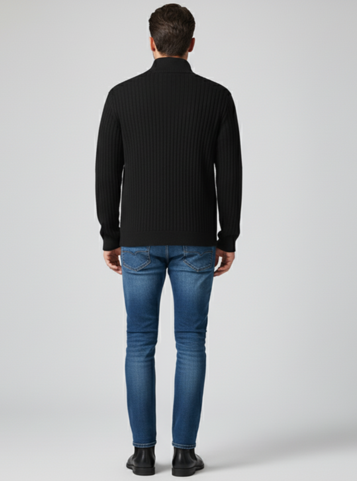 Man wearing a black ribbed sweater and blue jeans on a white background