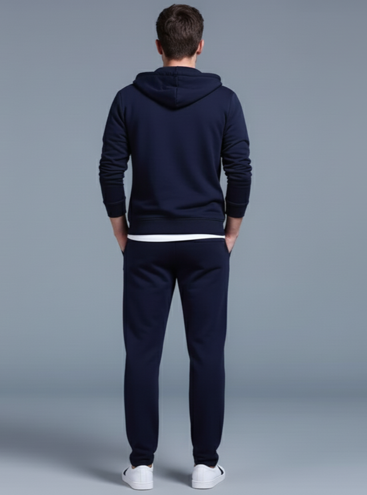 Man wearing a navy tracksuit with white shoes on a gray background