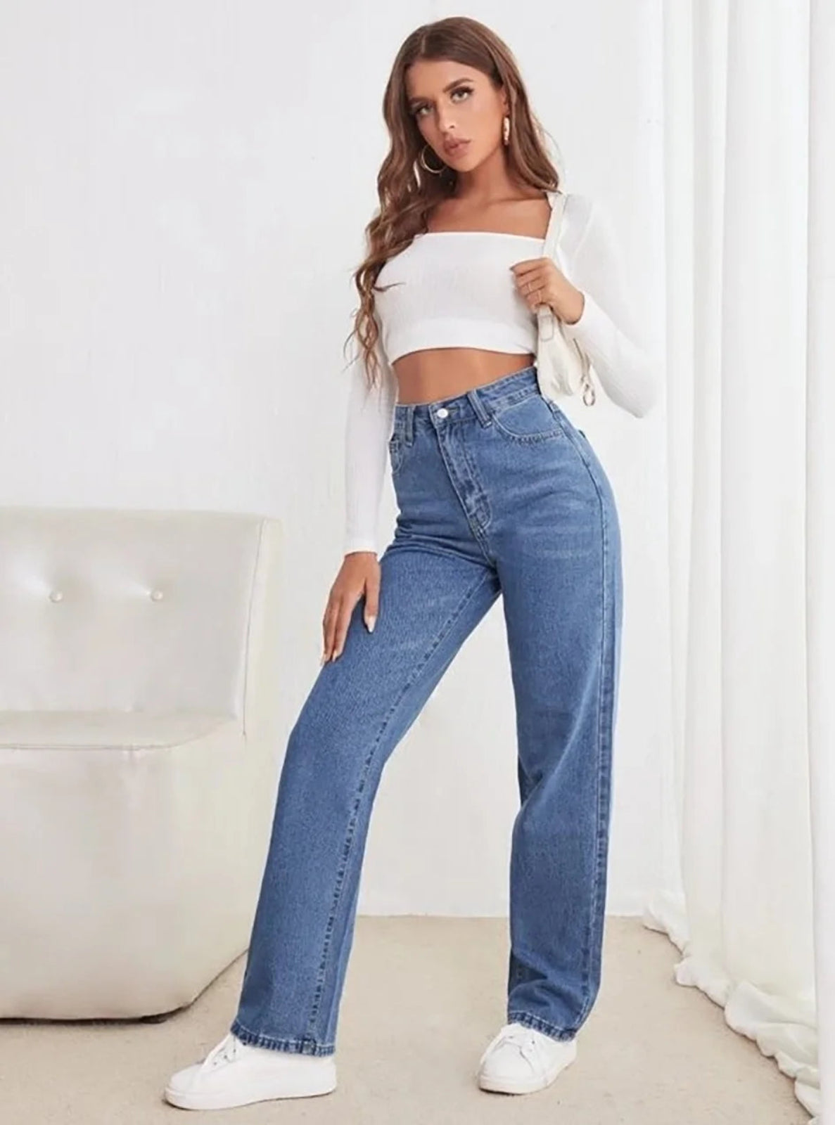 Woman wearing a white off-shoulder top and blue jeans indoors.