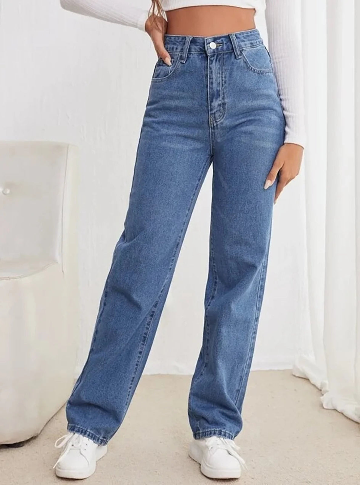 Person wearing blue jeans and white sneakers on a neutral background