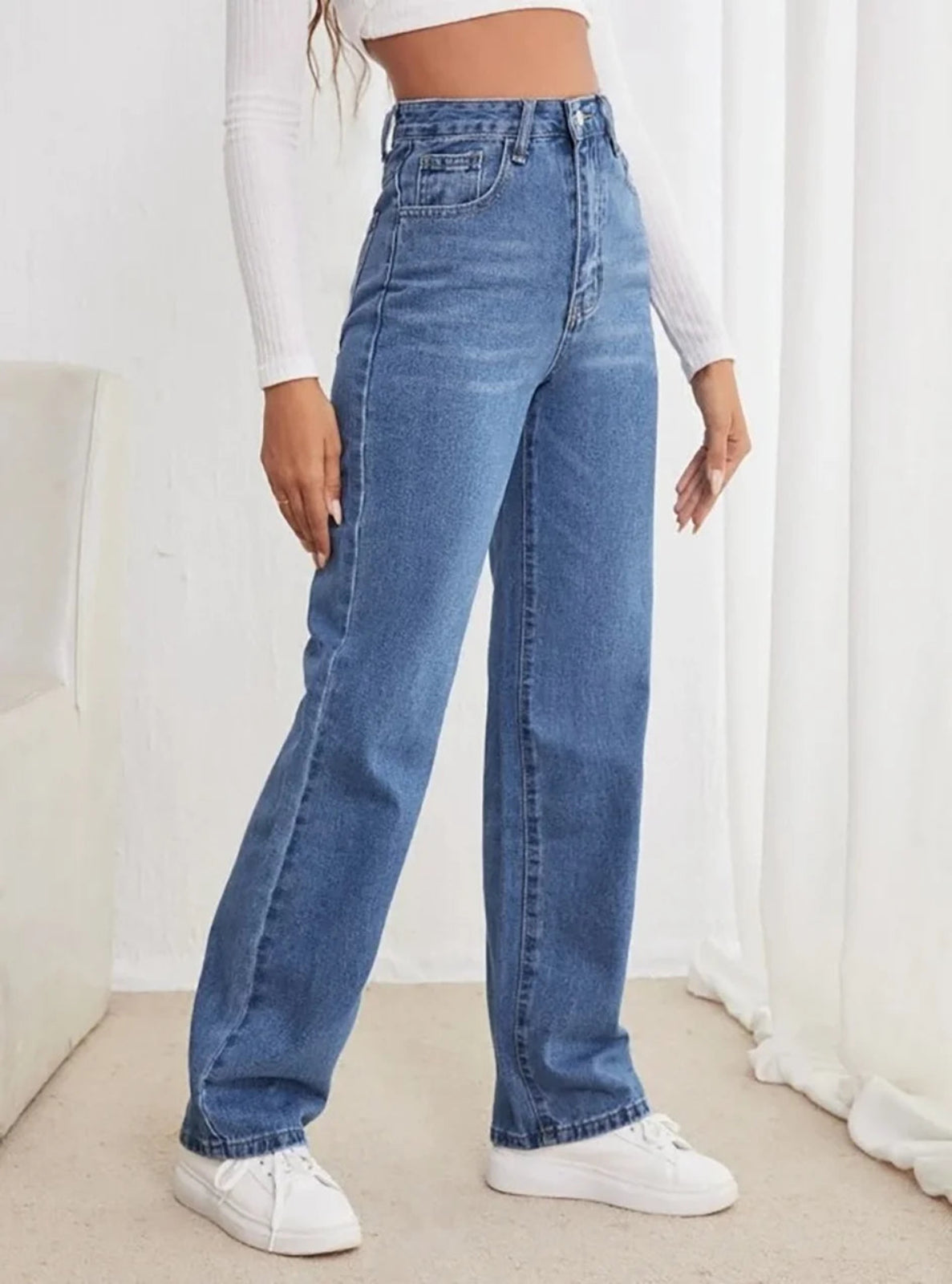 Person wearing blue jeans and white sneakers in a minimalistic setting