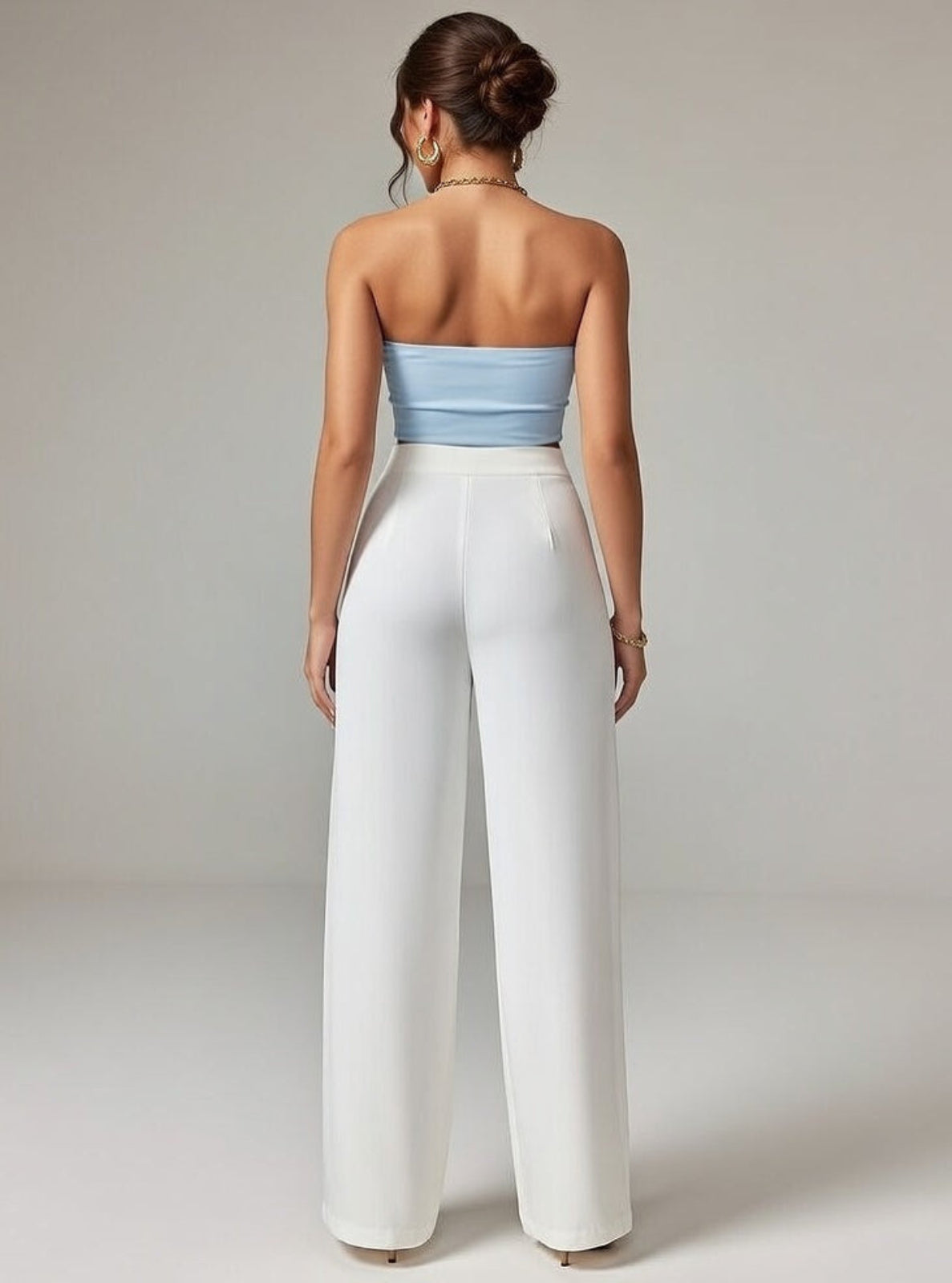 Woman wearing a strapless light blue top and white wide-leg pants on a plain background