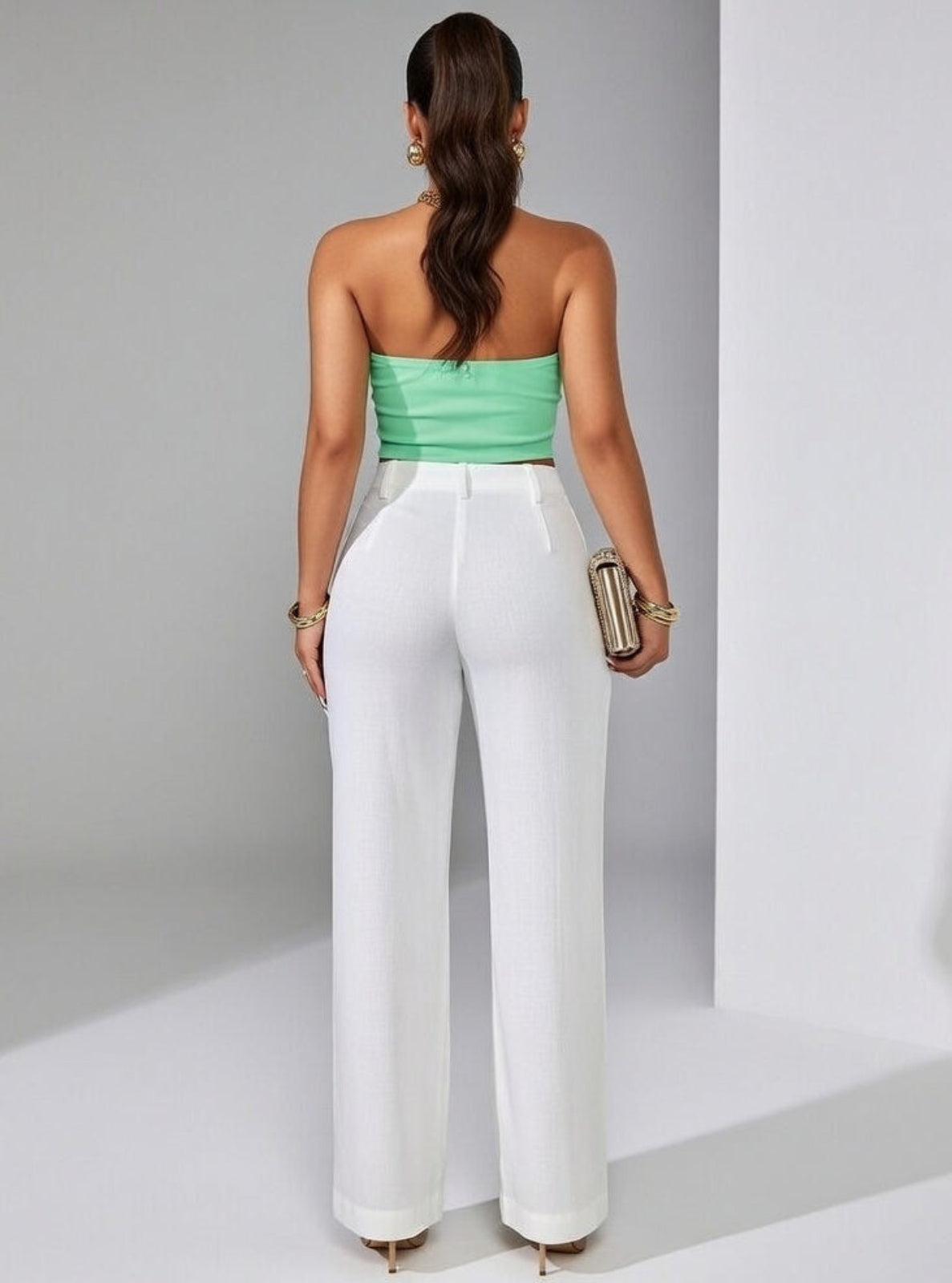 Woman wearing a green strapless top and white pants against a gray background