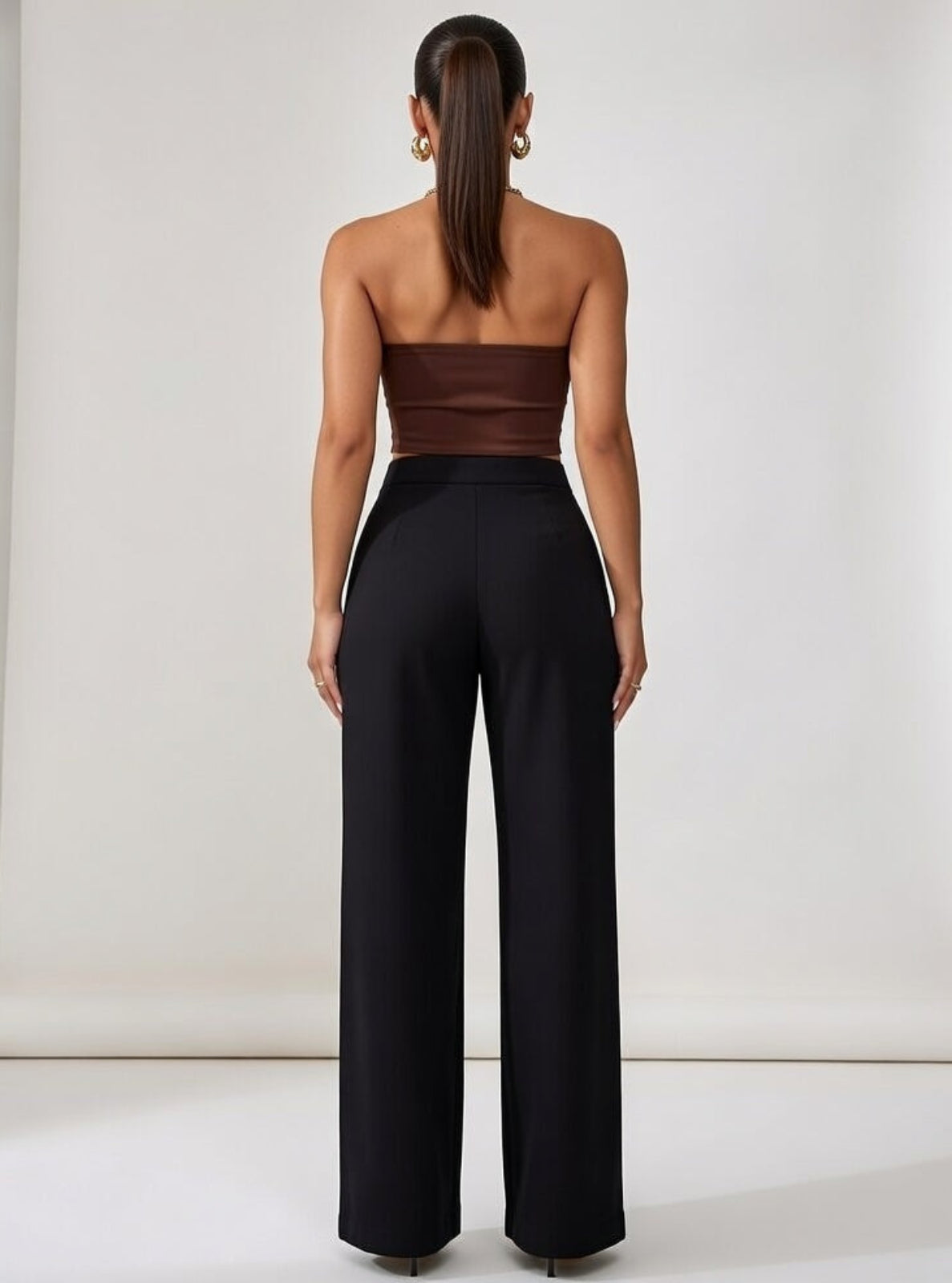 Woman wearing a brown strapless top and black high-waisted pants against a white background
