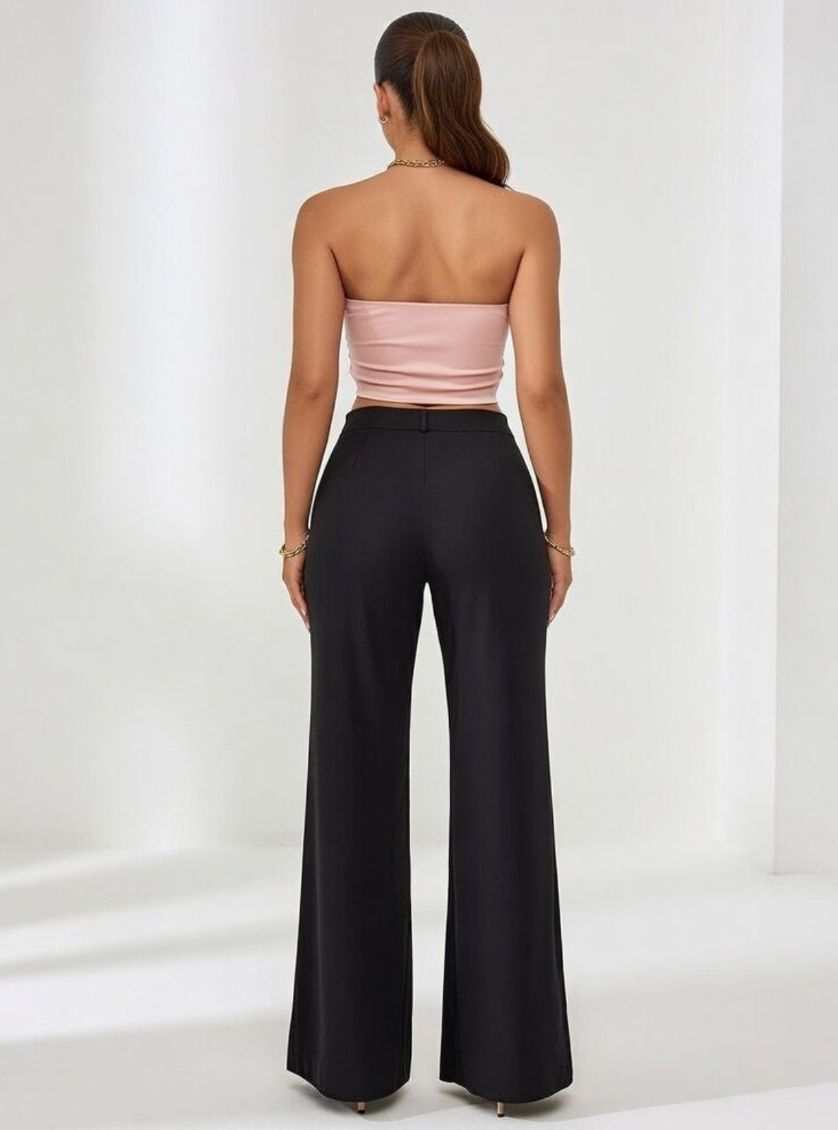 Woman wearing a strapless pink top and black high-waisted pants on a white background