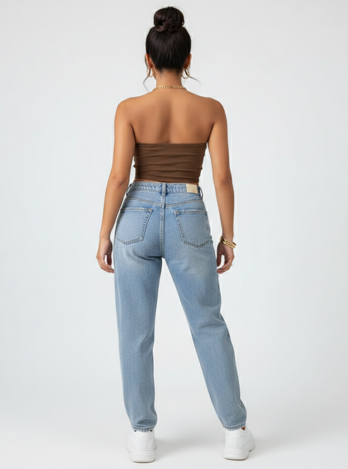 Woman wearing light blue jeans and a brown strapless top on a white background