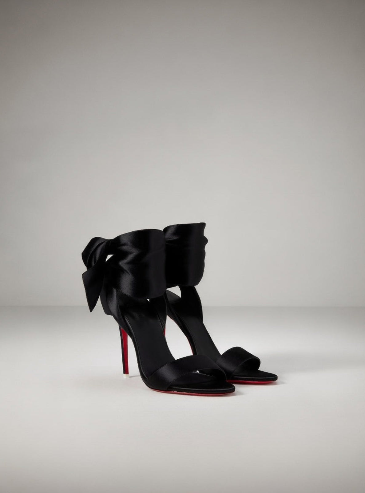 Black high-heeled shoes with large bows on a gray background