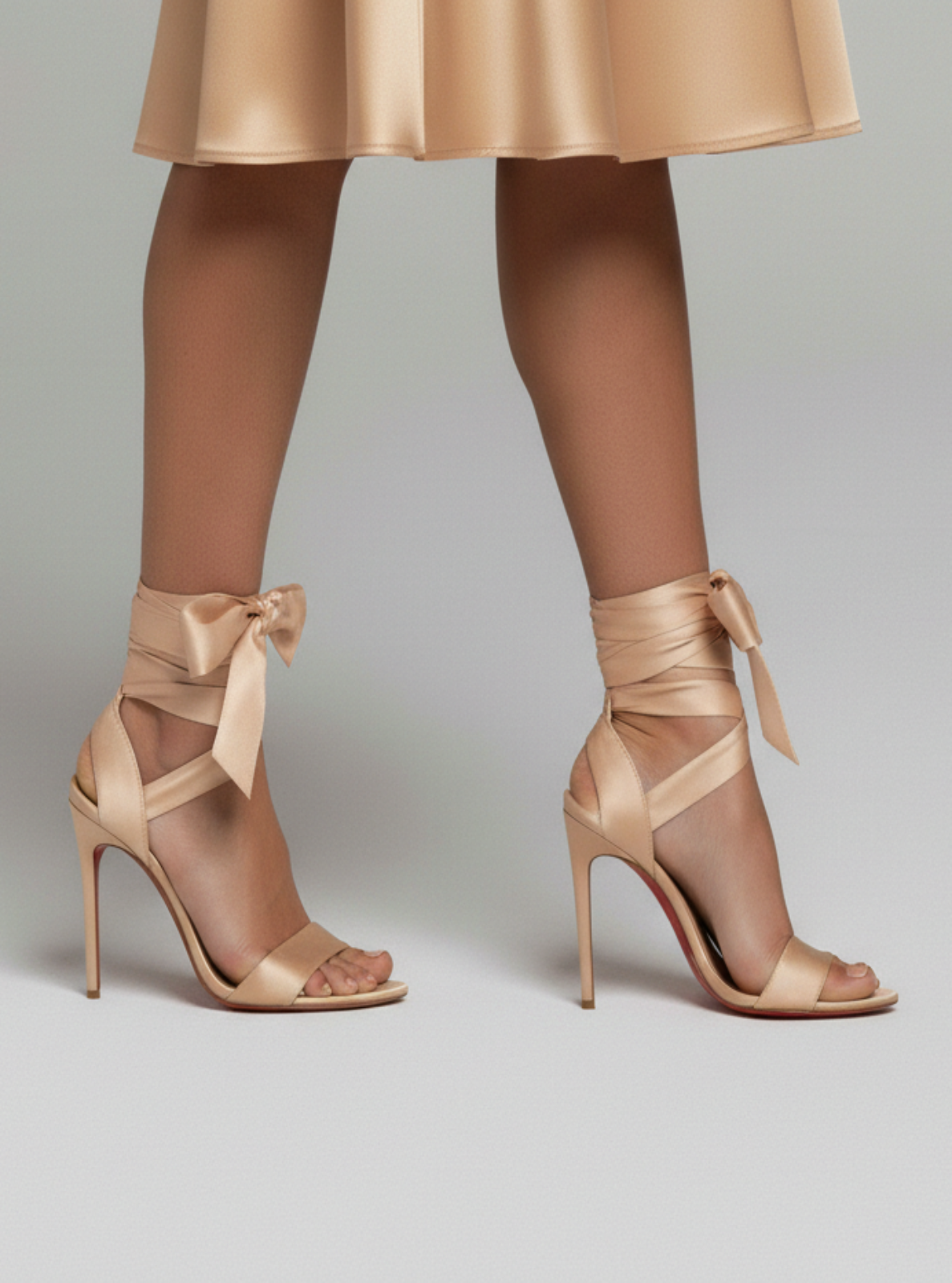 Beige high-heeled sandals with ribbon details worn with a beige skirt on a light gray background