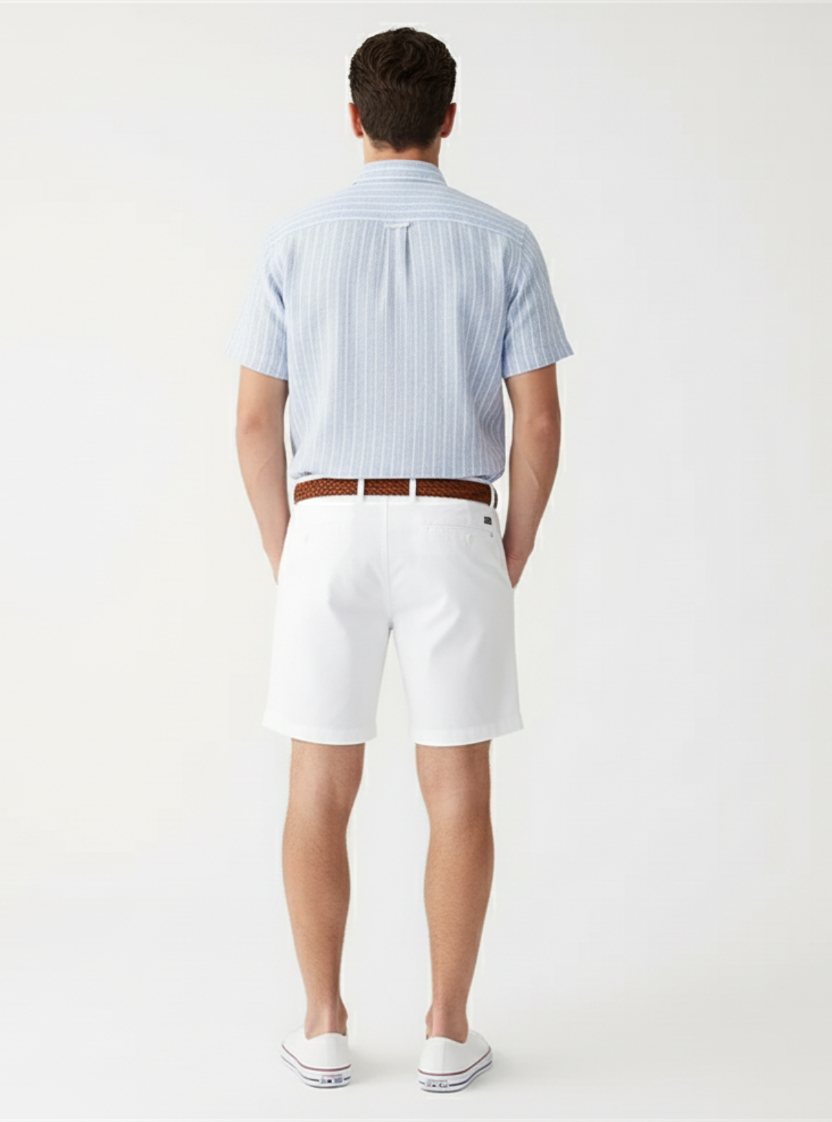 Man wearing a light blue striped shirt and white shorts on a plain background