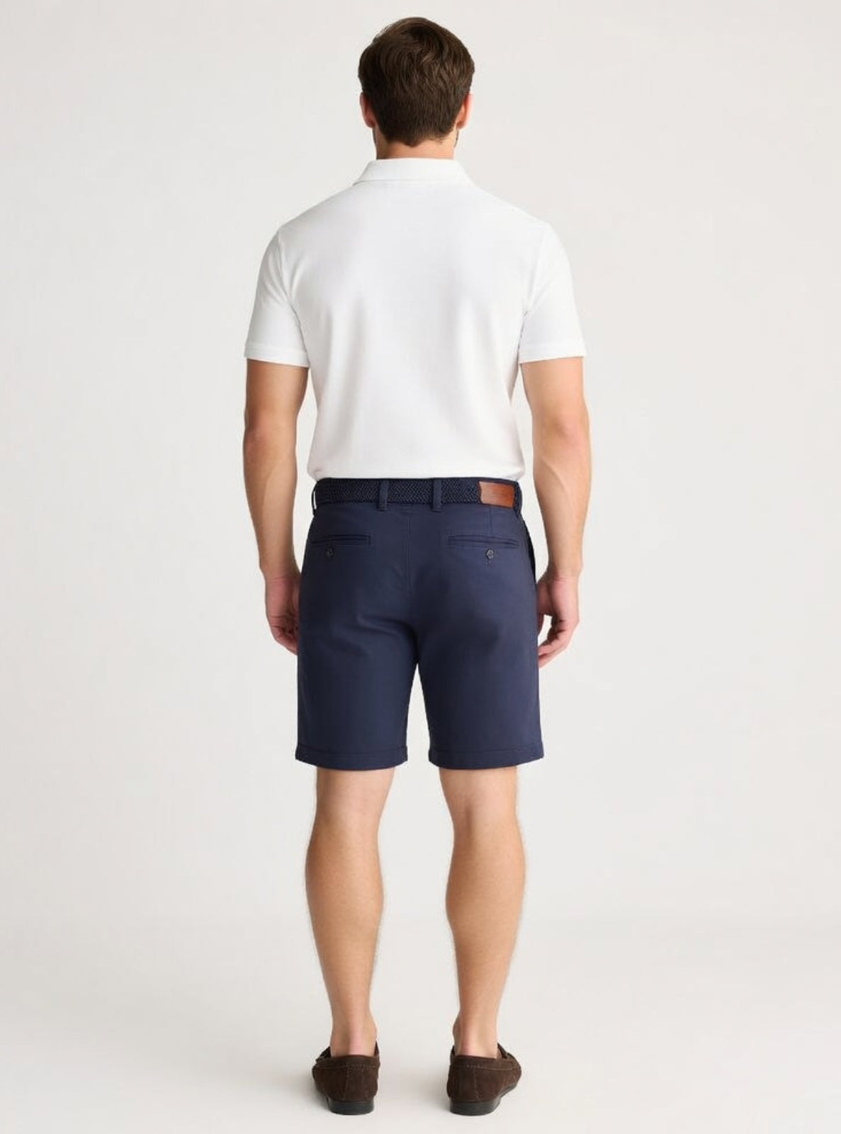 Man wearing navy shorts and a white shirt on a light gray background