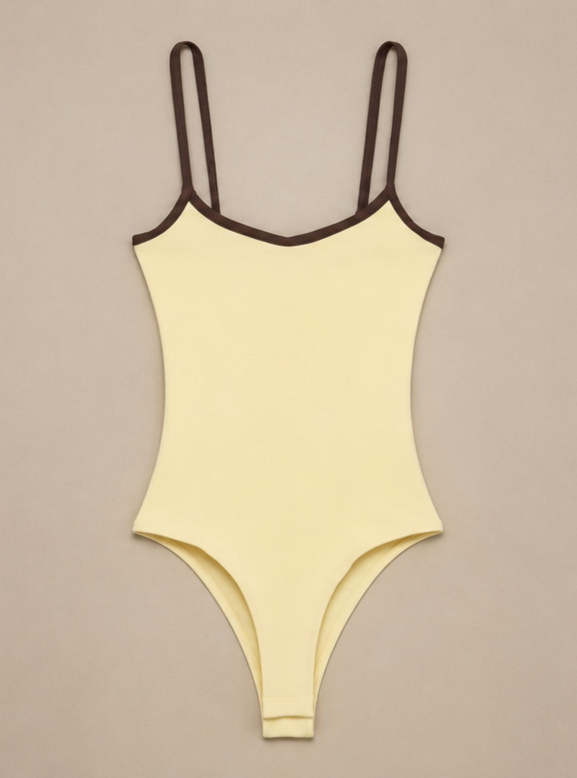 A pale yellow ribbed one-piece swimsuit with dark brown trim along the neckline and straps, displayed flat against a solid taupe background.