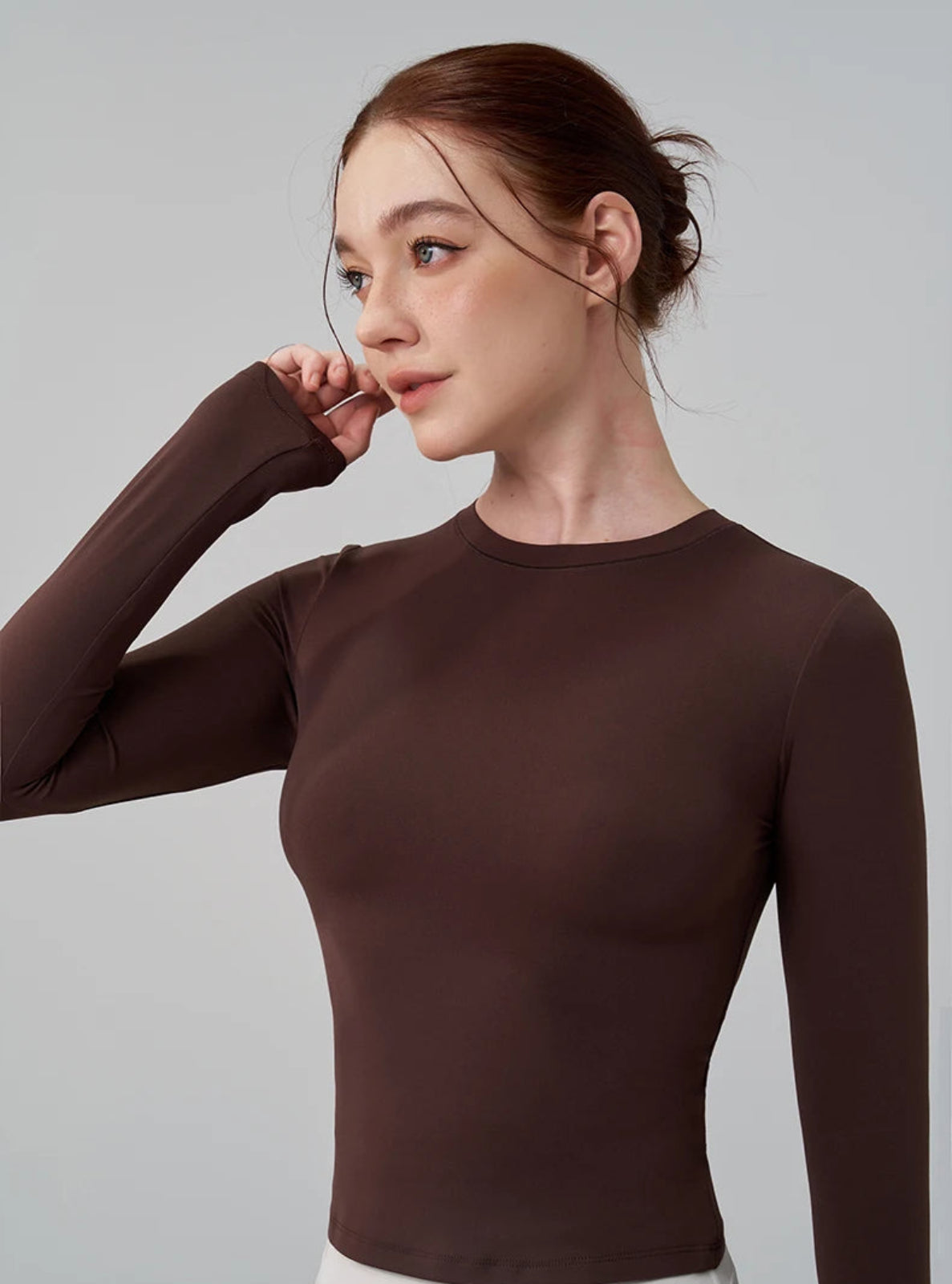 Woman wearing a brown long-sleeve top against a gray background