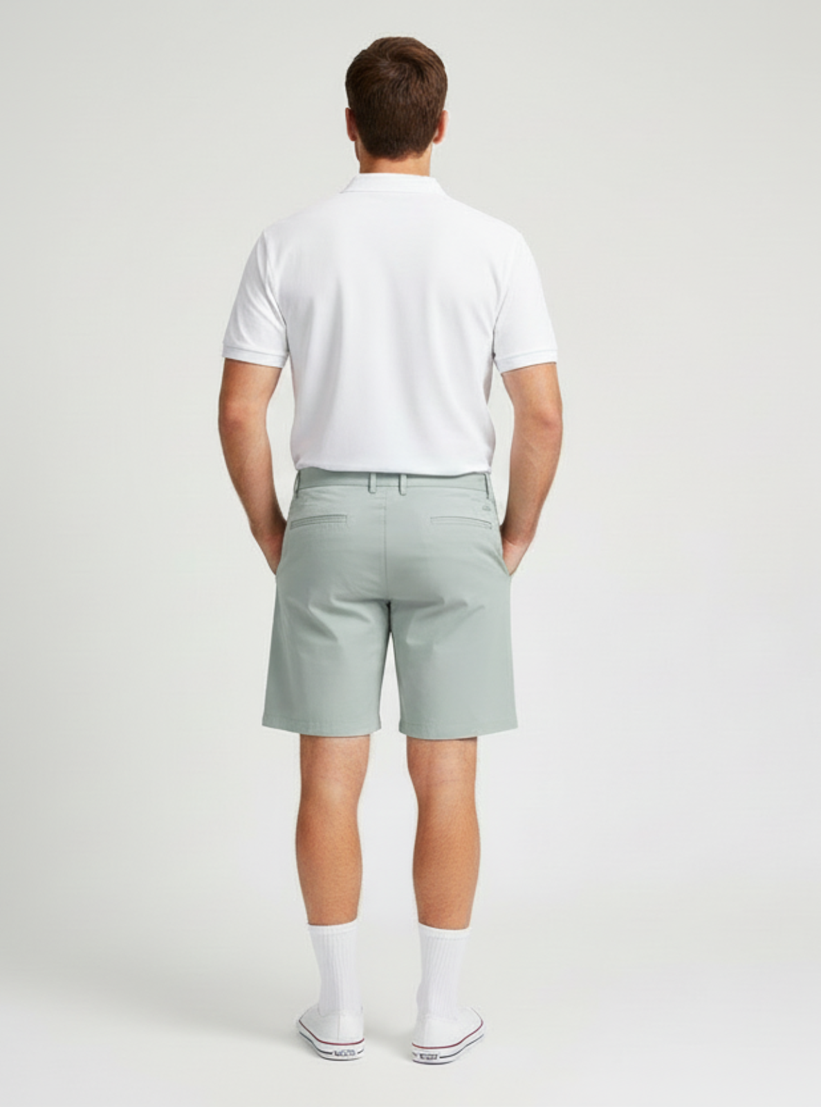 Man wearing a white polo shirt and light gray shorts on a plain background