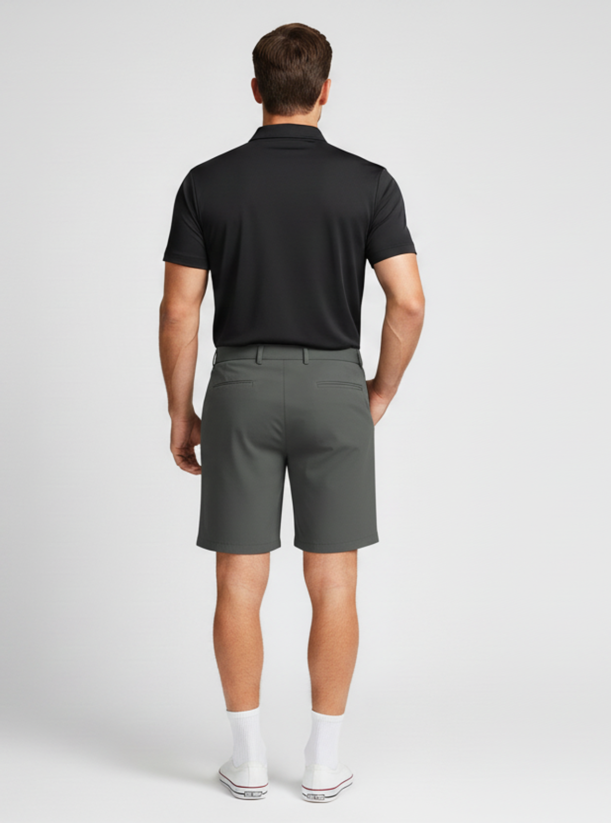 Man wearing a black polo shirt and gray shorts on a white background