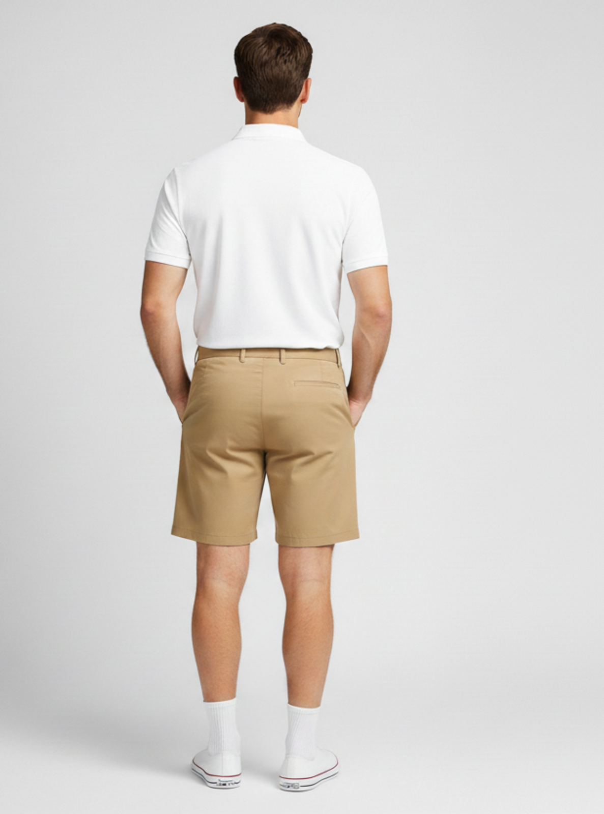 Man wearing a white polo shirt and beige shorts on a gray background