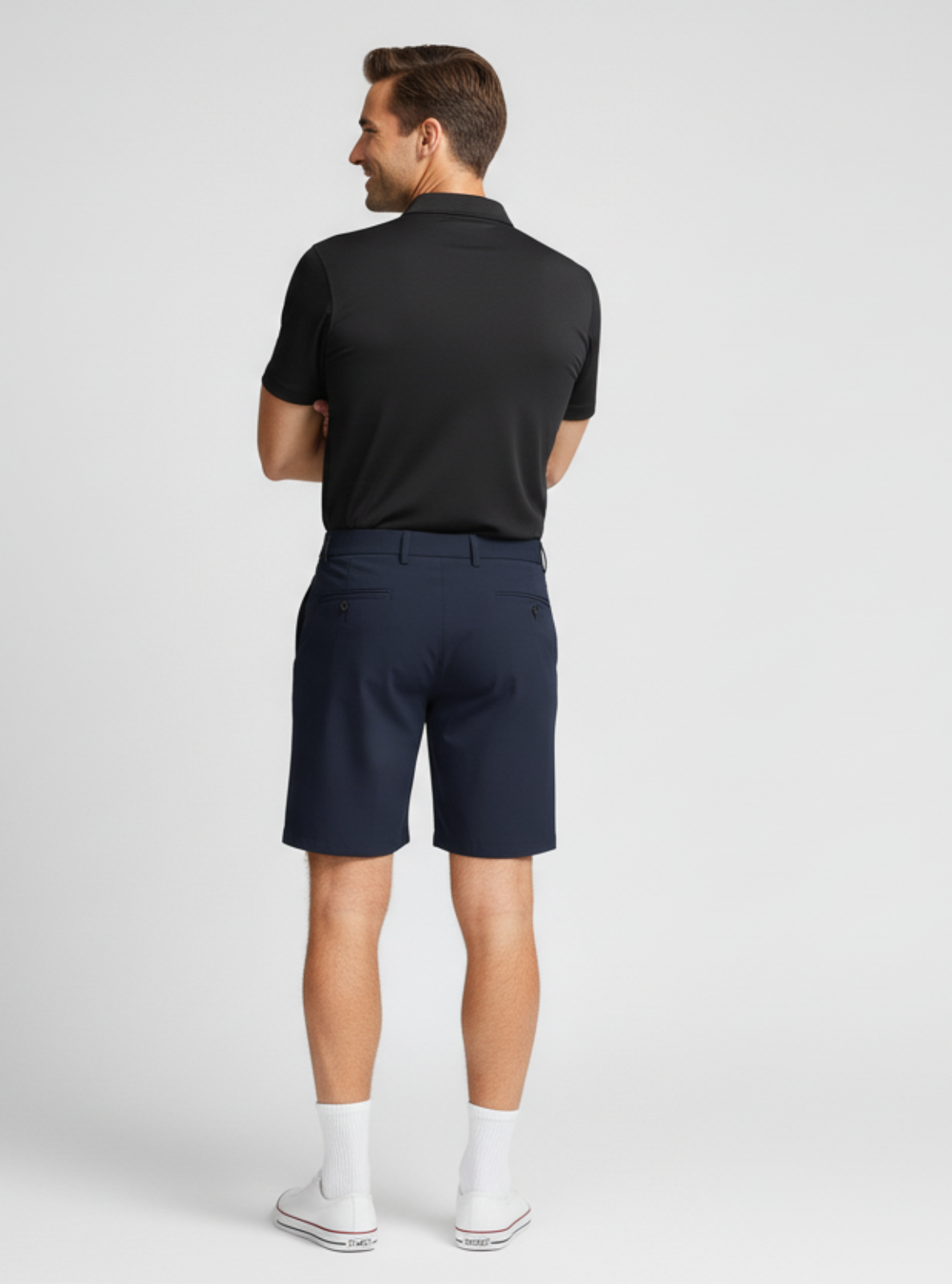 Man wearing a black polo shirt and navy shorts on a white background