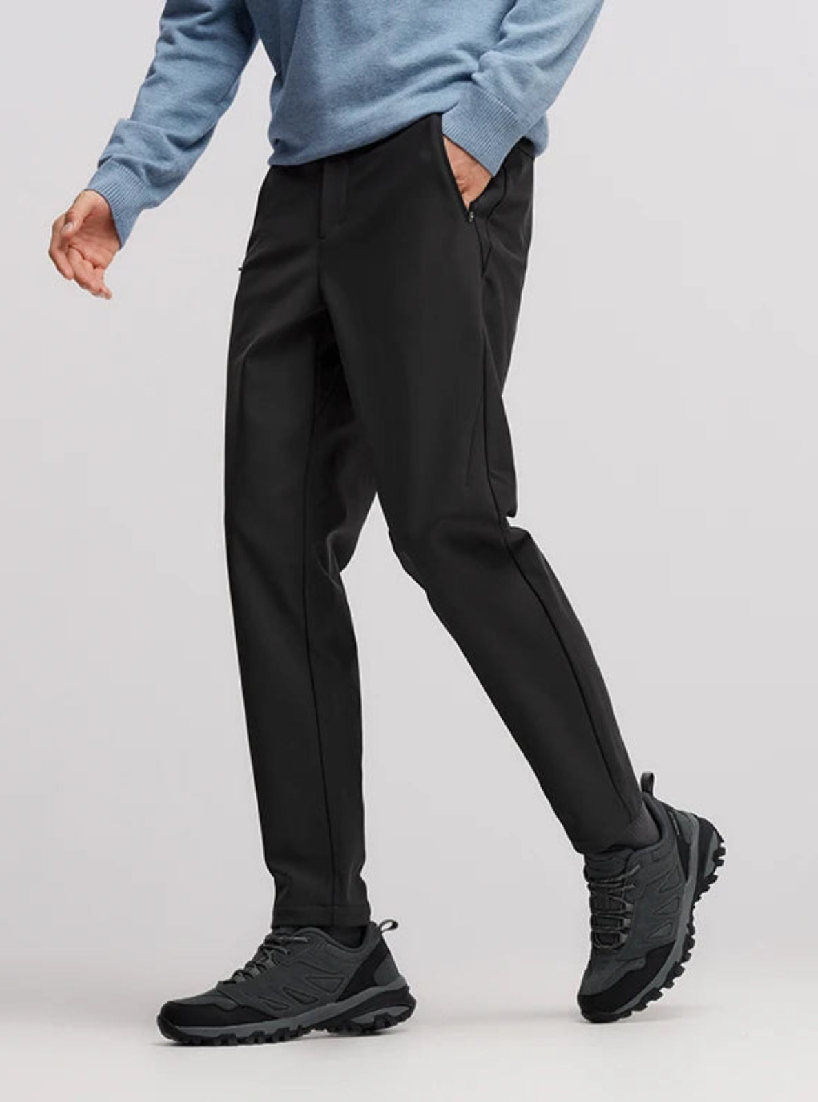 Person wearing black pants and black shoes on a light gray background