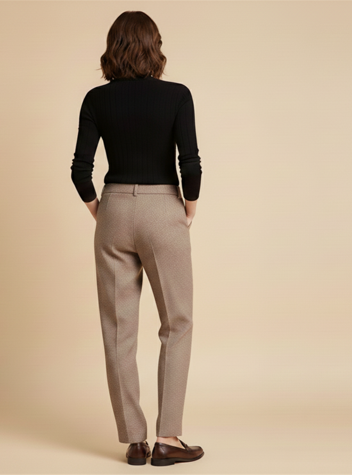 Person wearing a black top and beige pants on a beige background