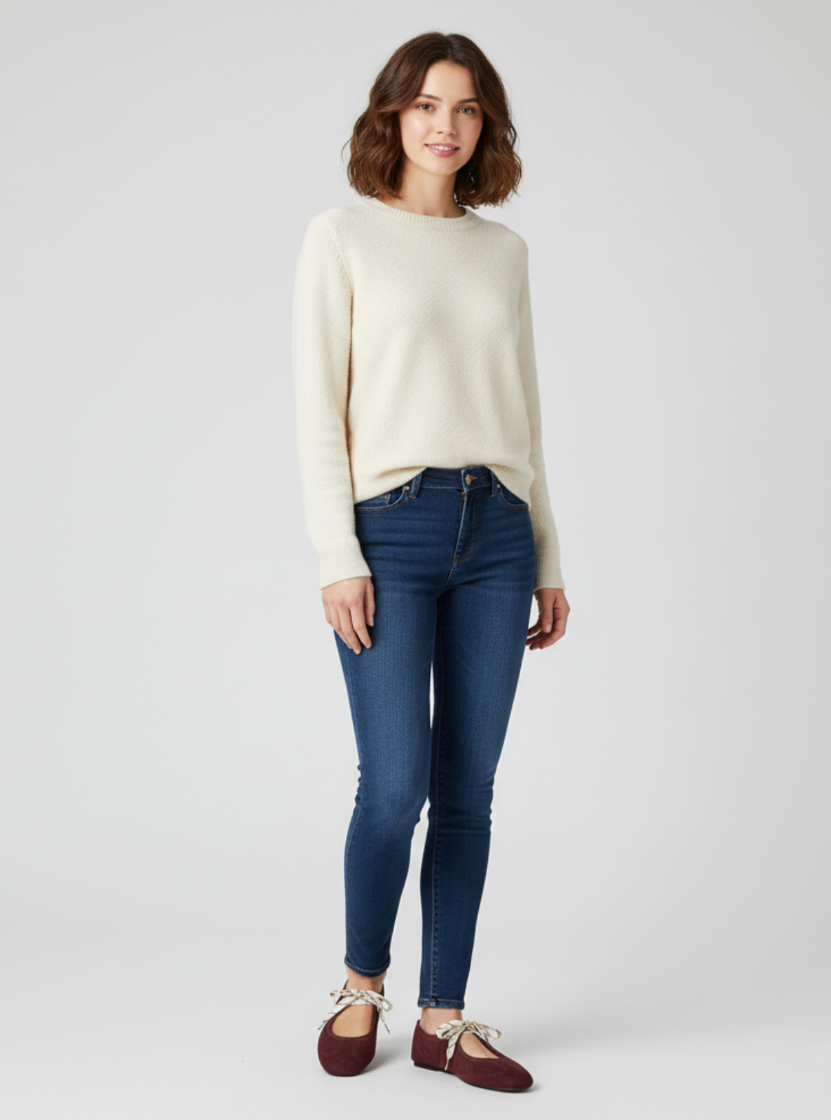 Woman wearing a cream sweater and blue jeans on a white background