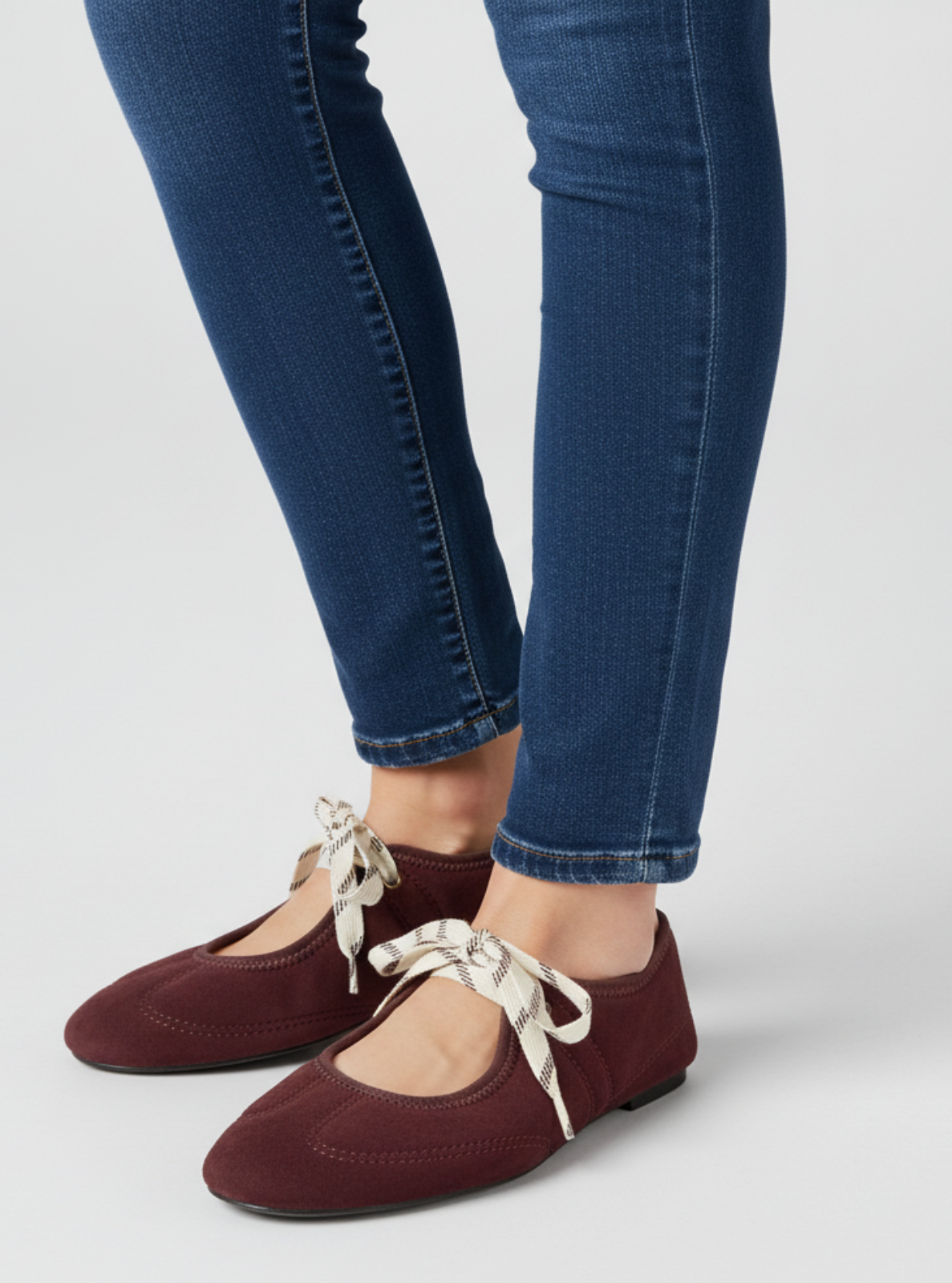 Maroon shoes with white laces worn with blue jeans on a light gray background