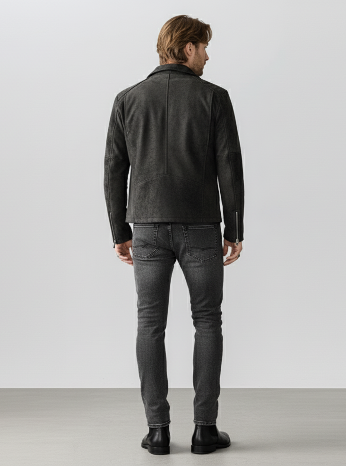 Man wearing a black leather jacket and jeans standing against a white background