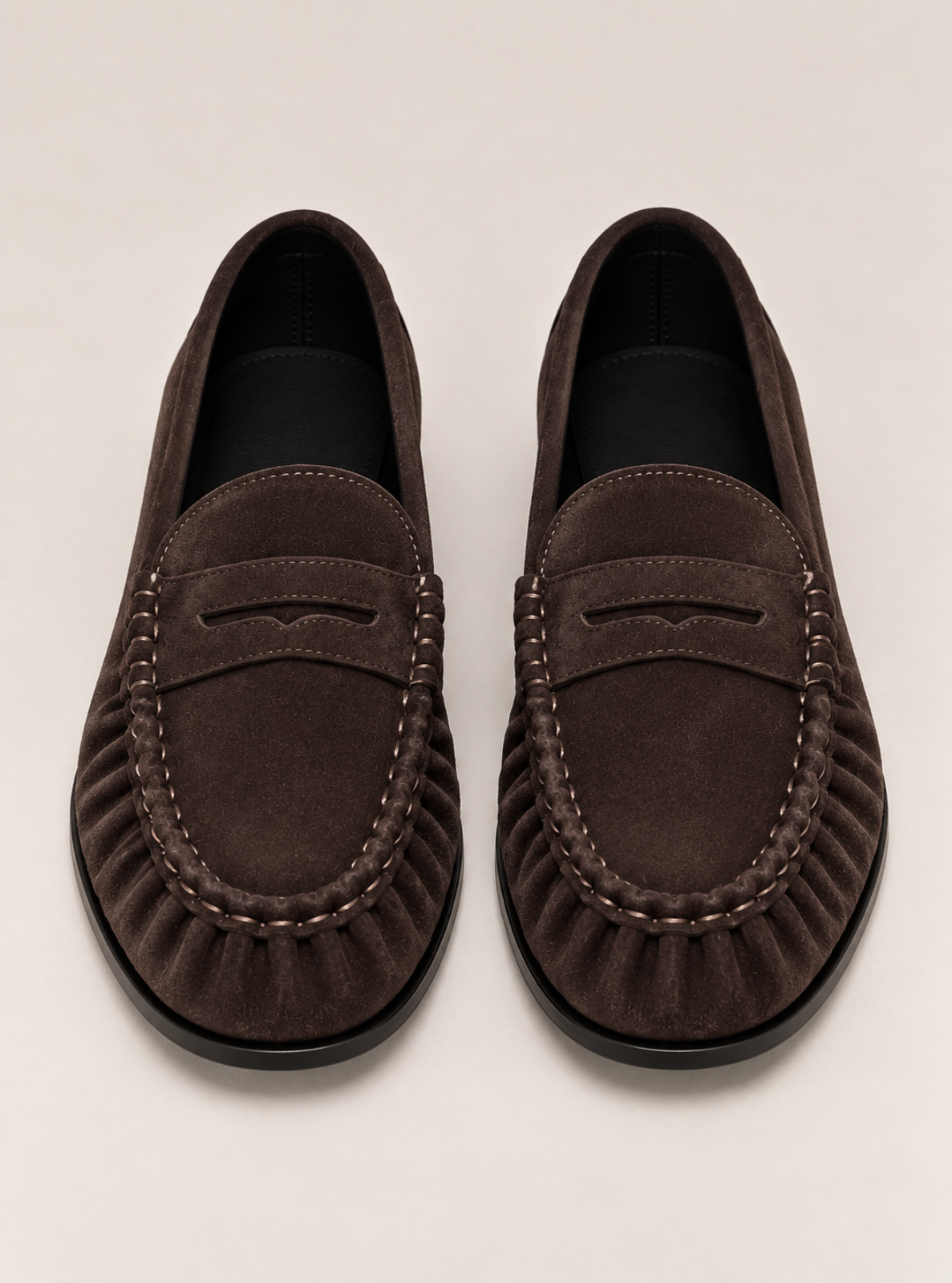 A pair of dark brown suede penny loafers with decorative stitching and a ruffled front, shown from a top-down view on a light beige background.