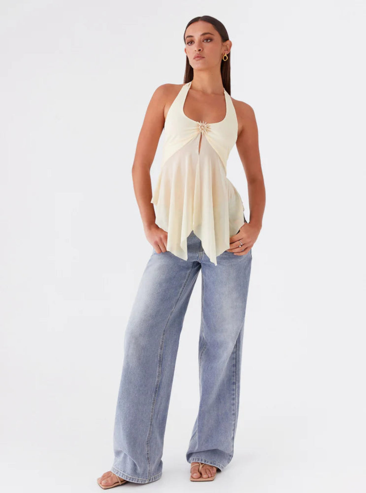 Woman wearing a white sleeveless top and light blue jeans on a white background