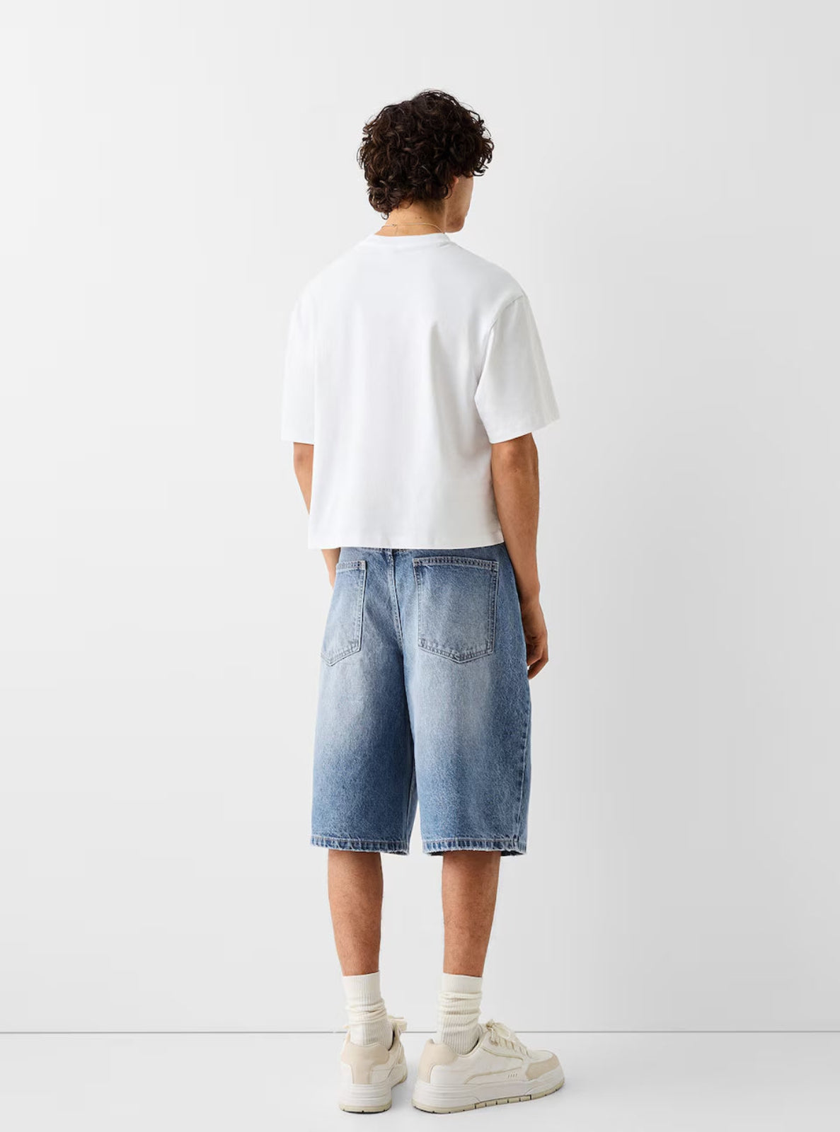 Person wearing a white t-shirt and blue denim shorts on a plain background