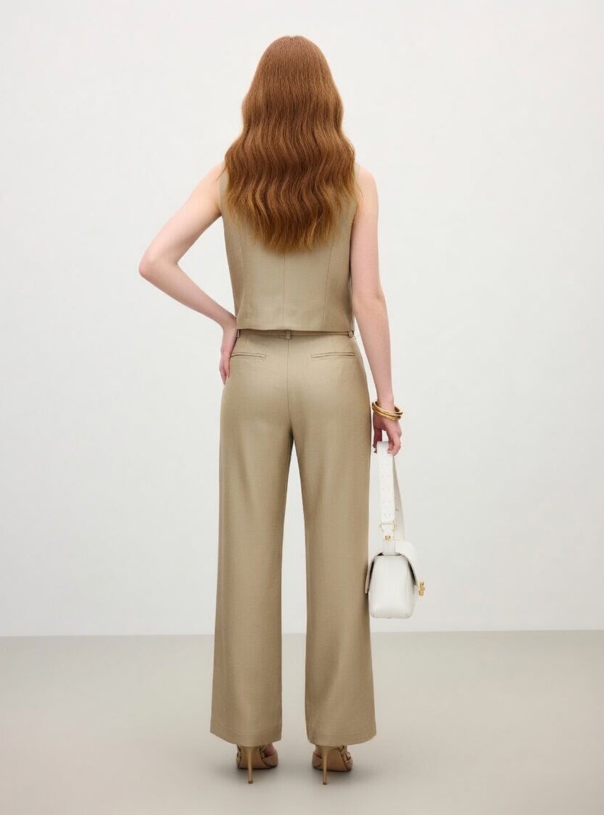 Woman wearing a beige sleeveless top and wide-leg pants against a white background